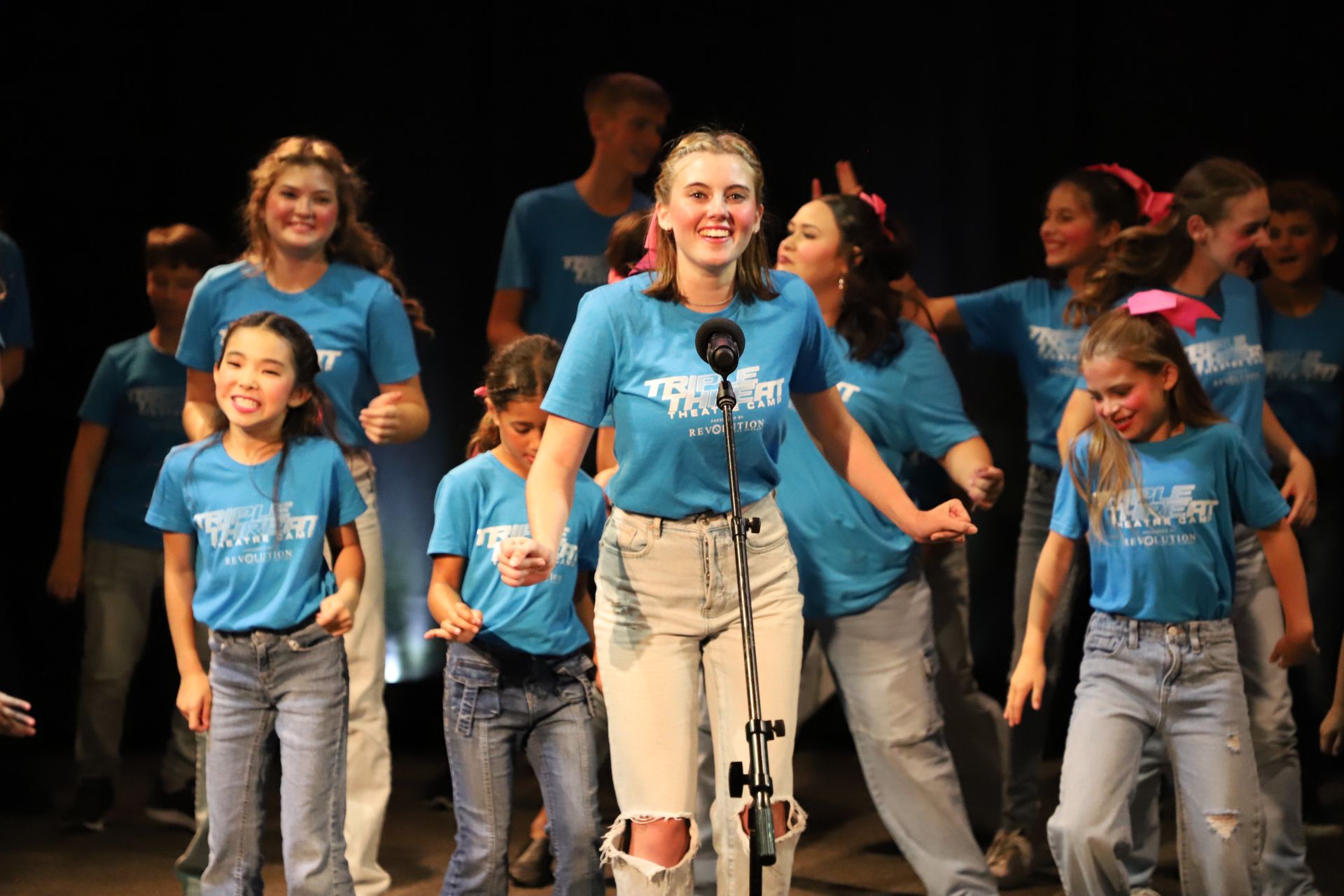 A group of young girls in blue shirts are dancing on a stage.
