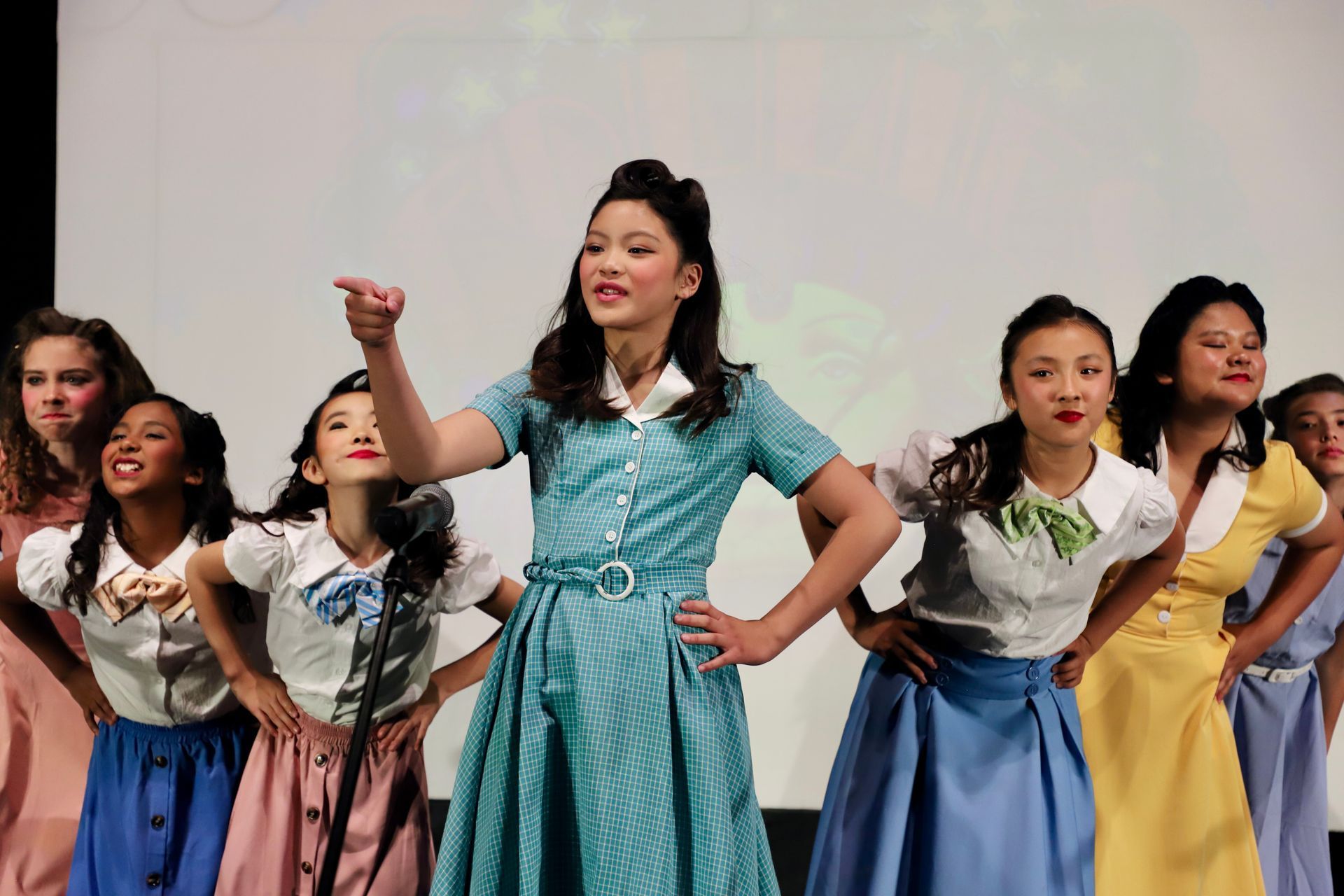 Women in colorful dresses performing a dance onstage with raised arms for a theater performance.