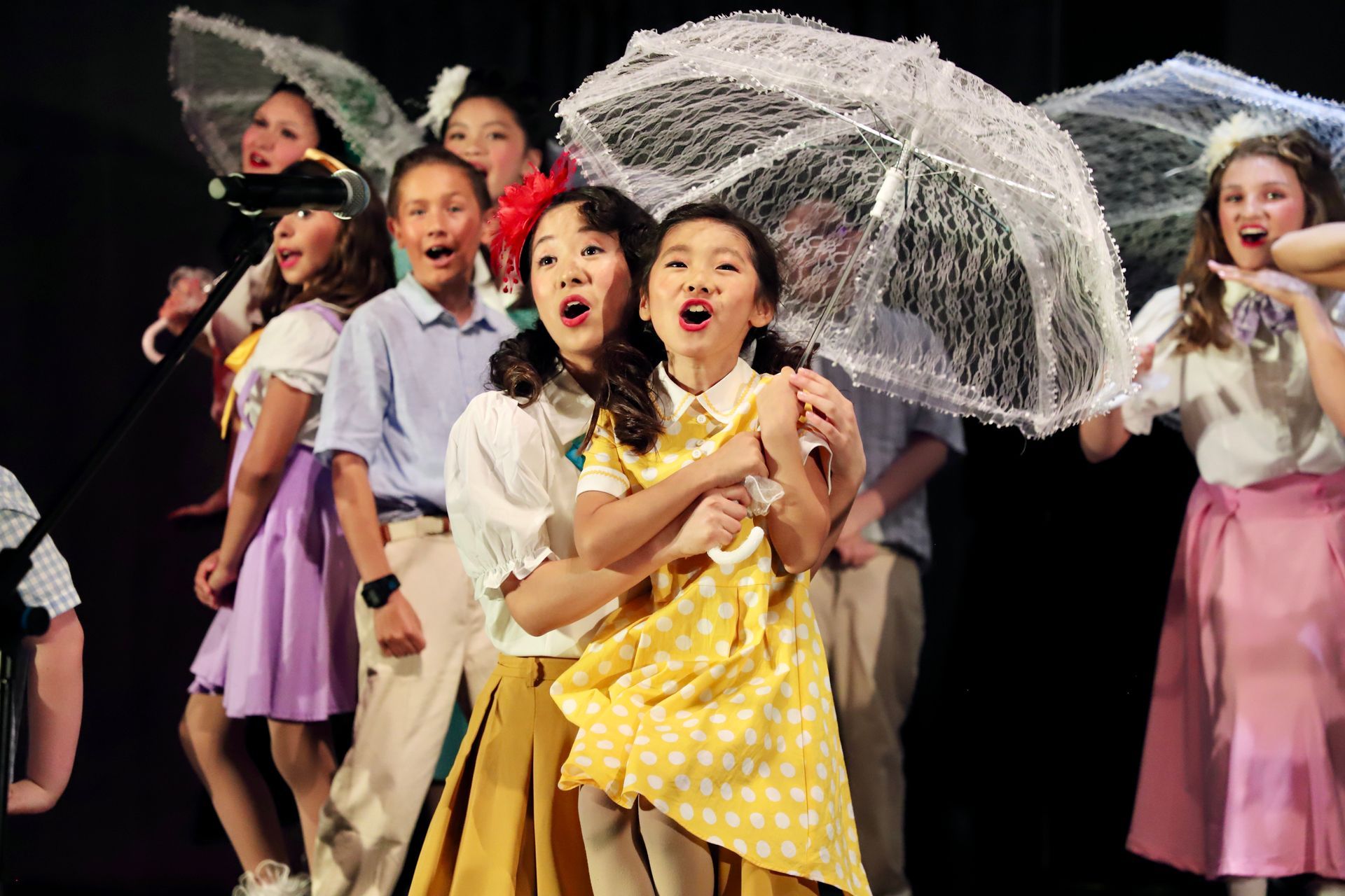 Children performing on stage, smiling and holding umbrellas in a colorful dance scene for a theater performance.