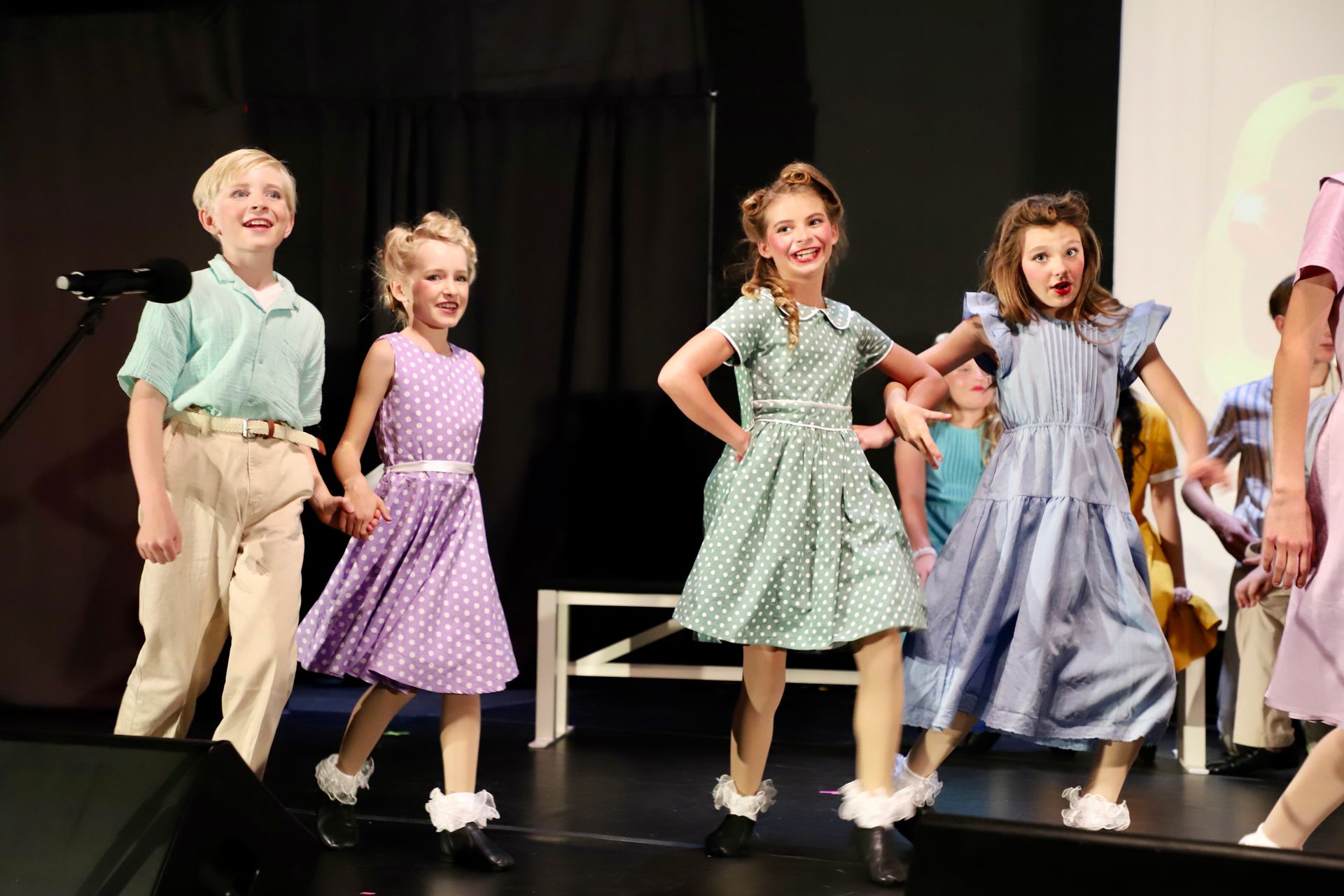Children performing a dance onstage in colorful costumes for a theater performance.