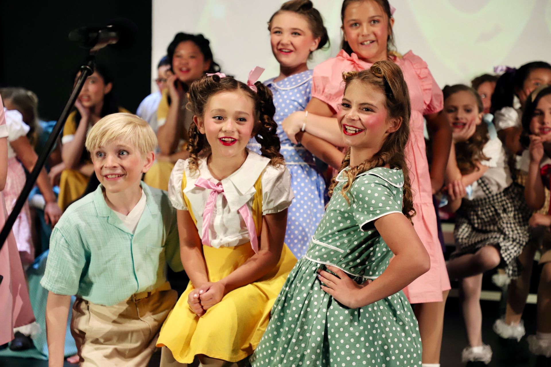 Children posing on a runway, smiling in colorful clothes and costumes for a theater performance.