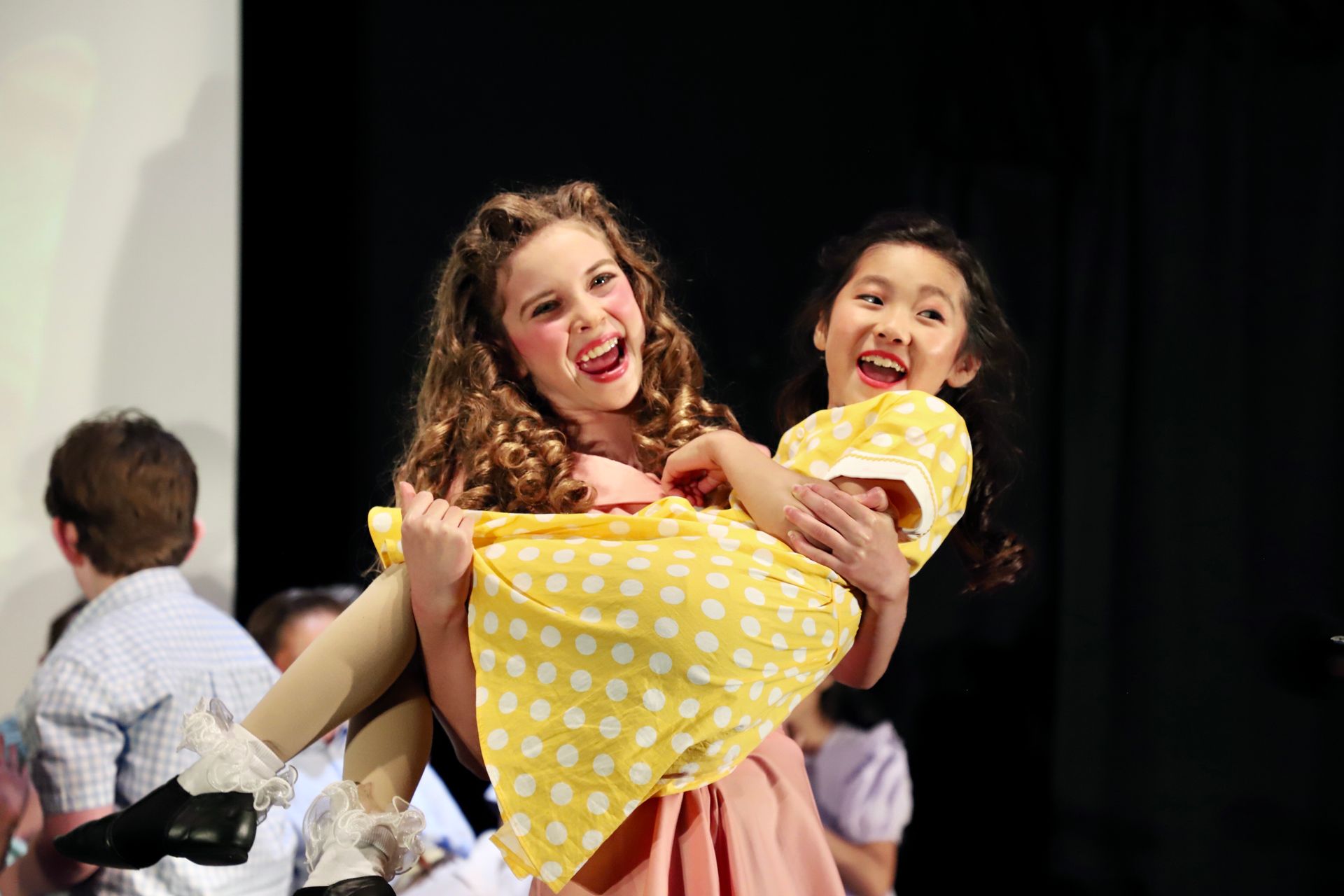 Two performers smiling and posing with a child onstage against a dark backdrop for a theater performance.