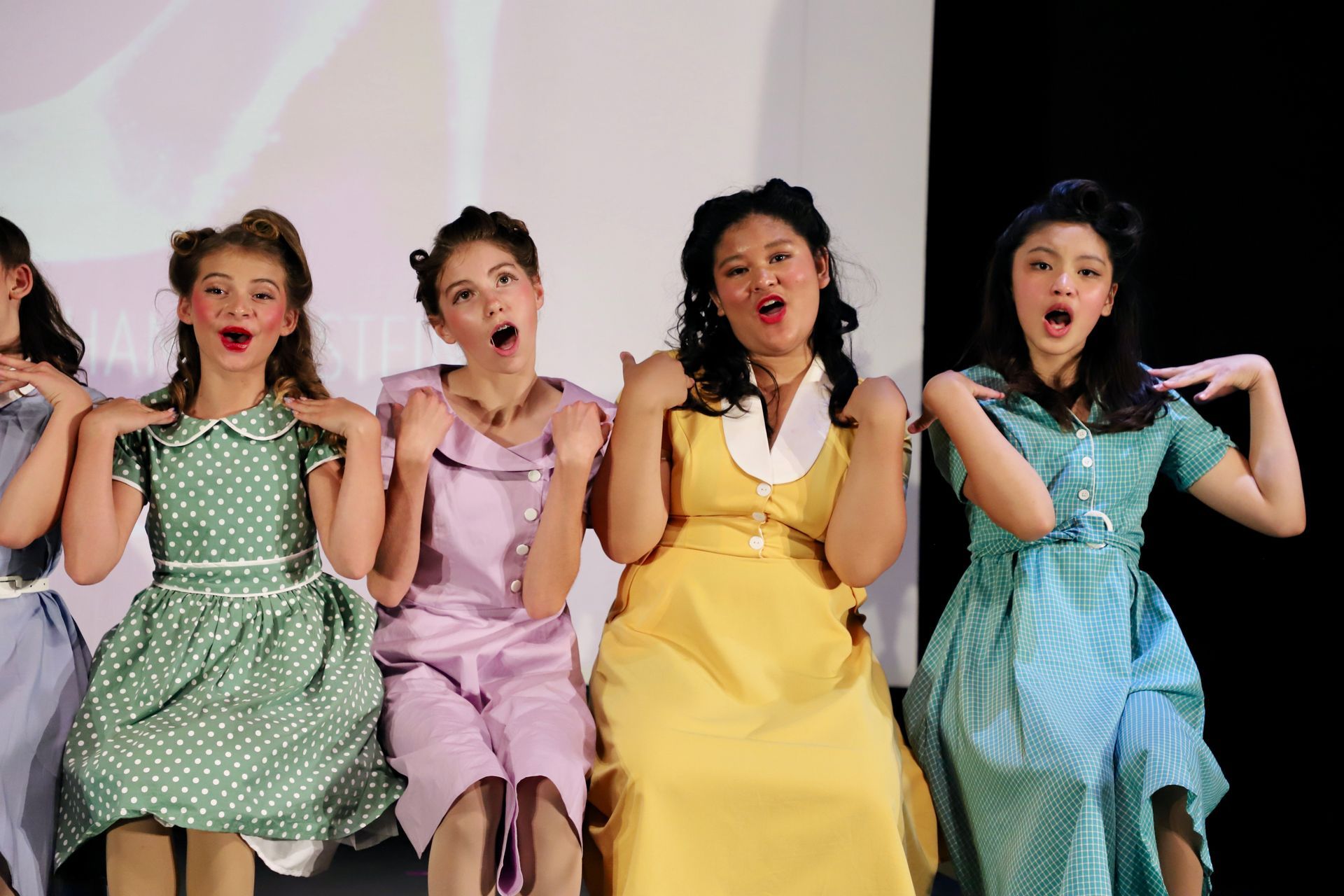Four performers in colorful dresses posing and singing on stage for a theater performance.