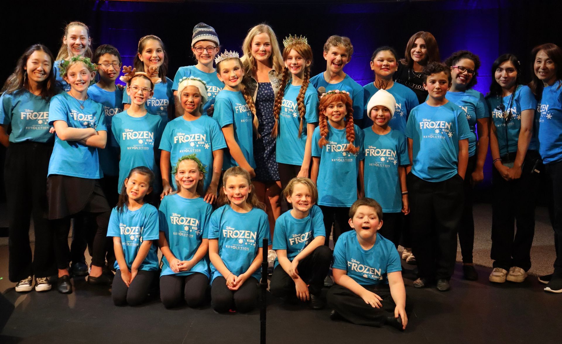A group of children wearing blue shirts are posing for a picture.
