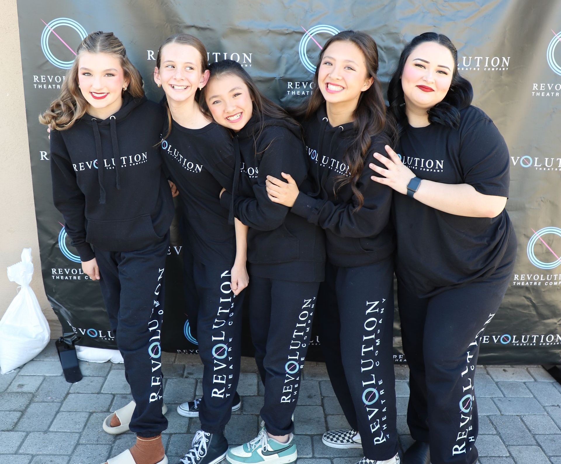 A group of young girls wearing black hoodies are posing for a picture.
