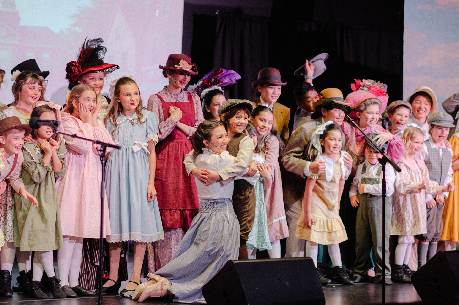 Children in colorful costumes singing and posing on a stage with microphones from The Music Man