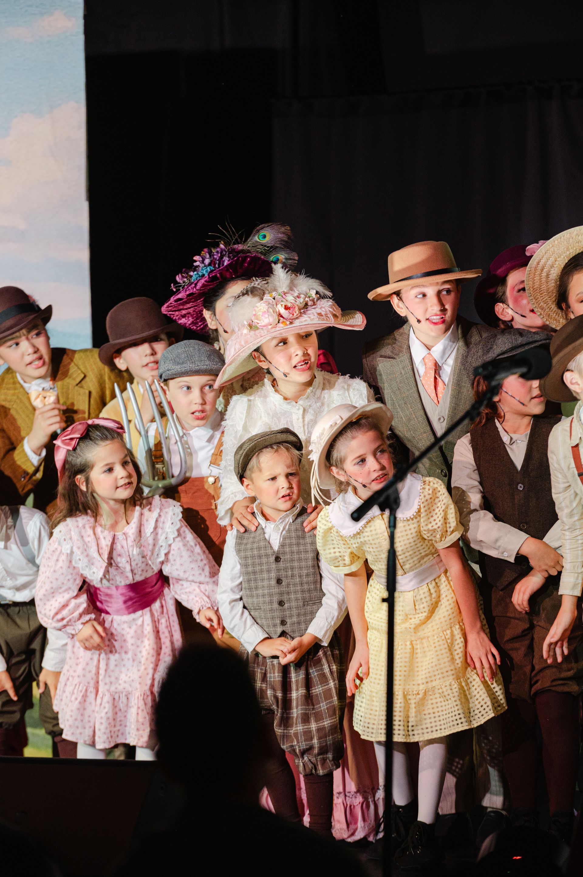 Children in vintage costumes performing onstage, with a microphone at center from The Music Man