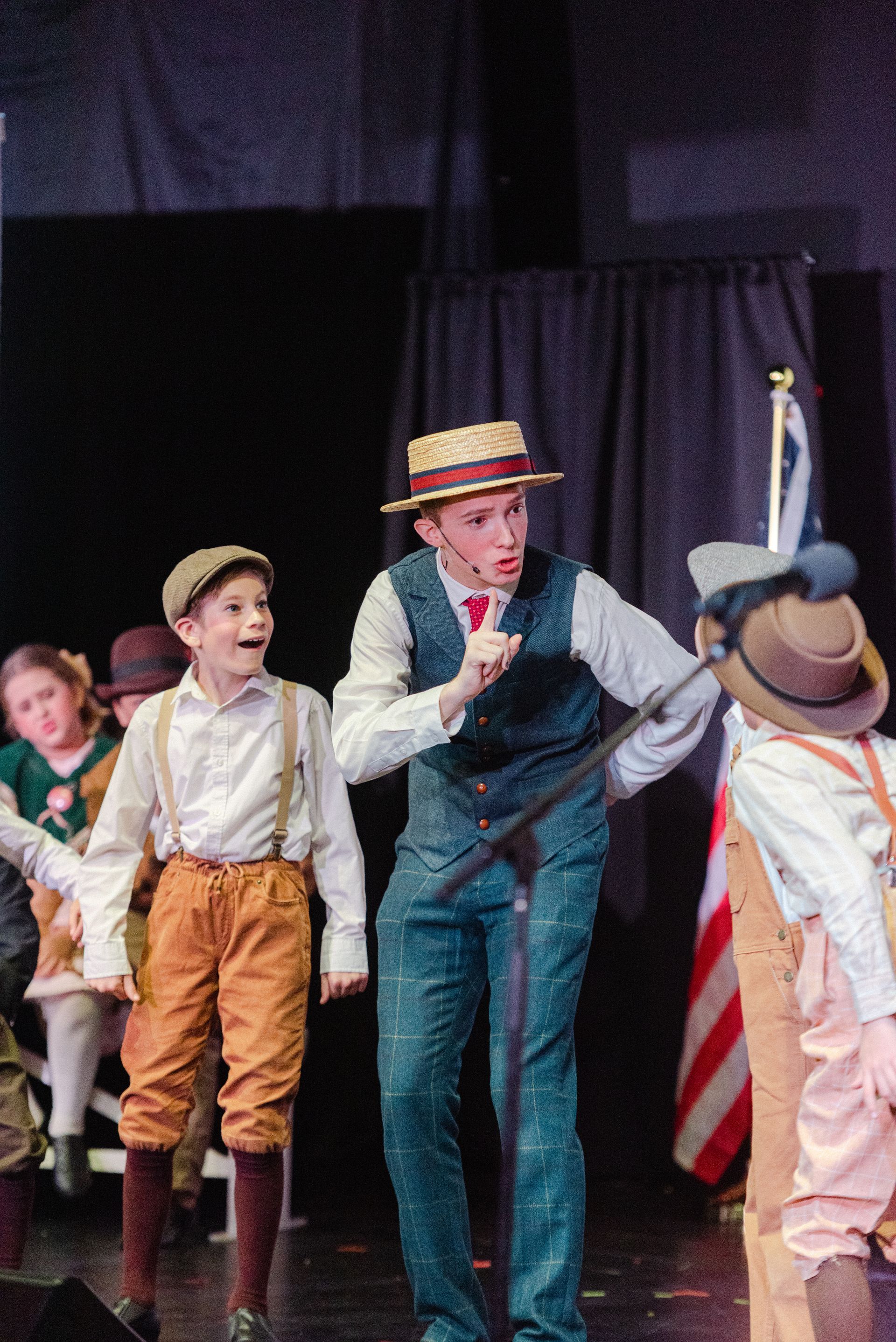 Children in costume performing on stage, with a central performer in a straw hat and blue vest from The Music Man