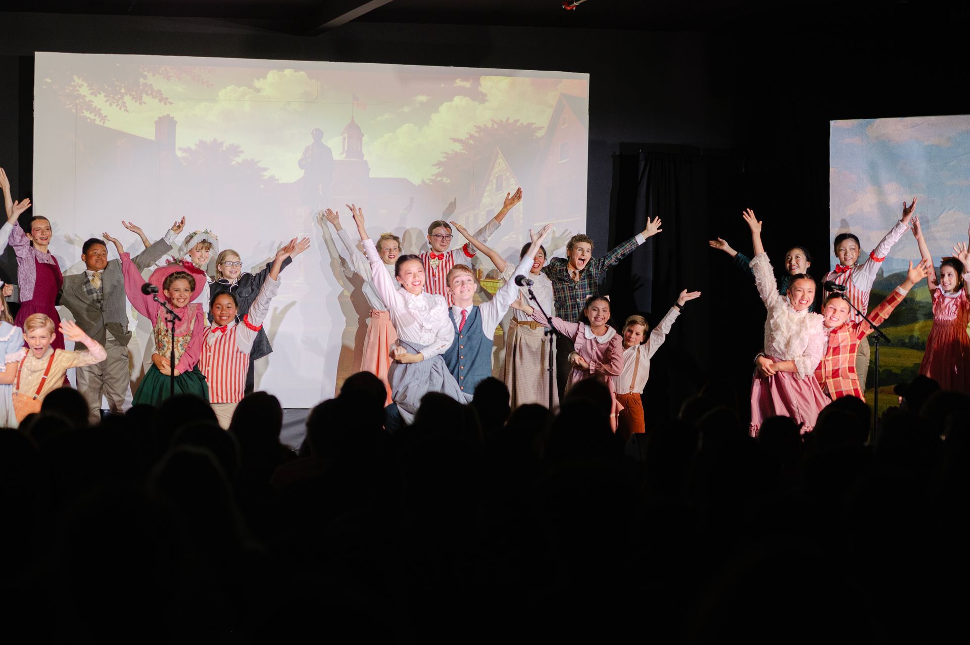 Performers in colorful costumes posing onstage with raised arms before a projected backdrop from The Music Man