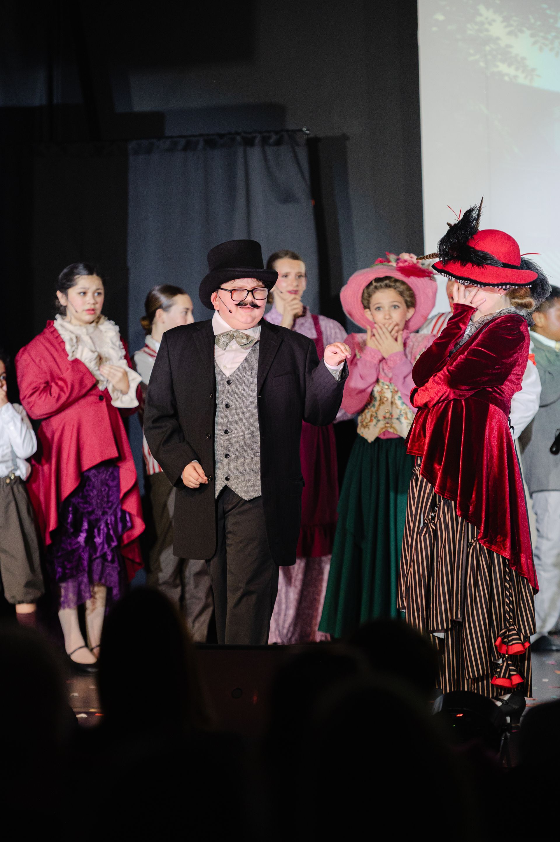Costumed performers onstage in colorful vintage outfits during a theatrical scene from The Music Man