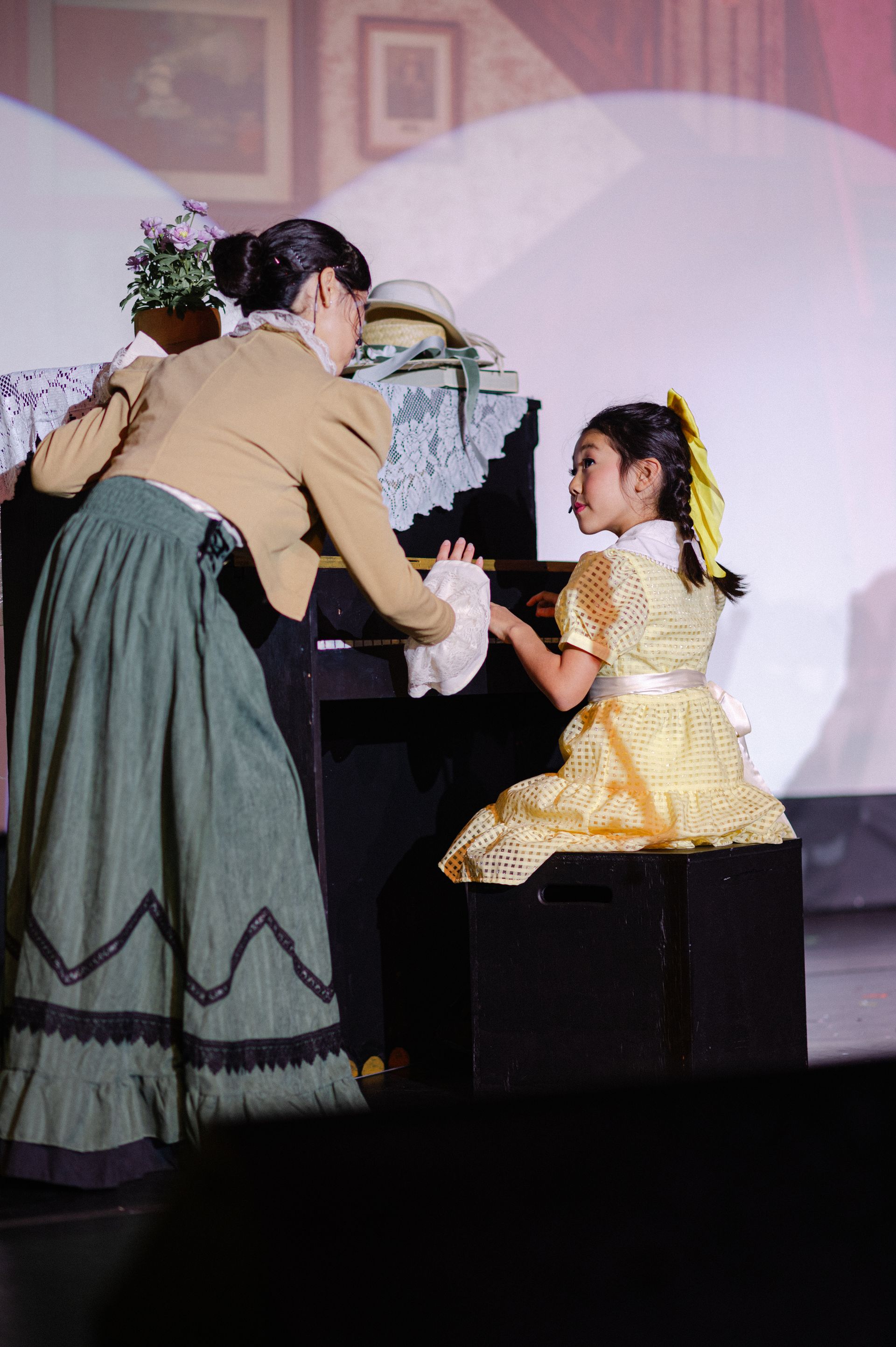 Two people on stage, one handing a small object to another in a yellow dress from The Music Man