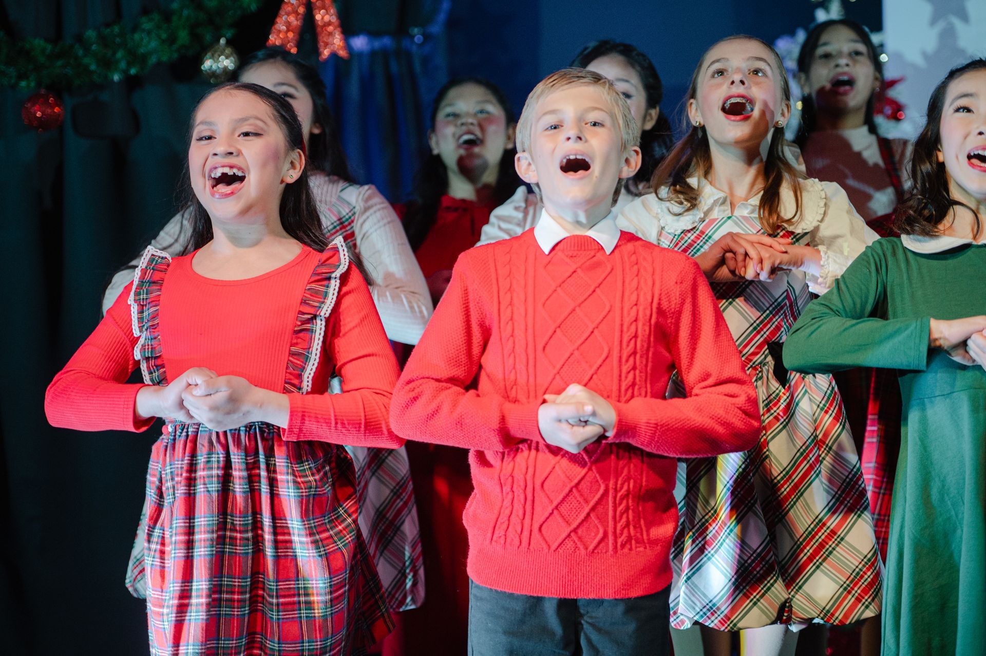 Children in red and festive outfits singing on a decorated stage
