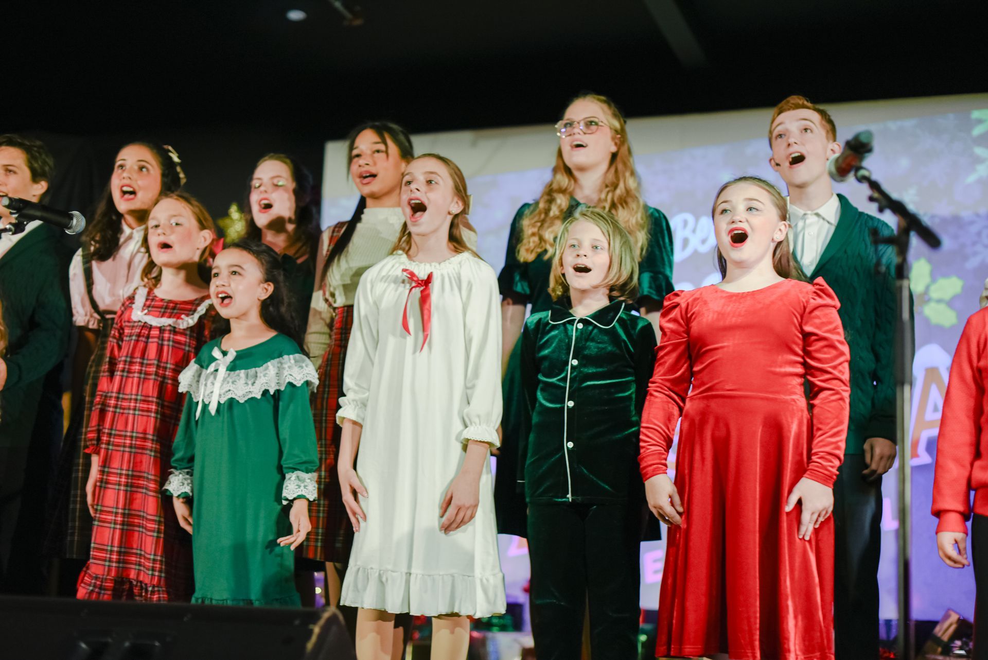 Children singing on stage in festive dresses during a performance