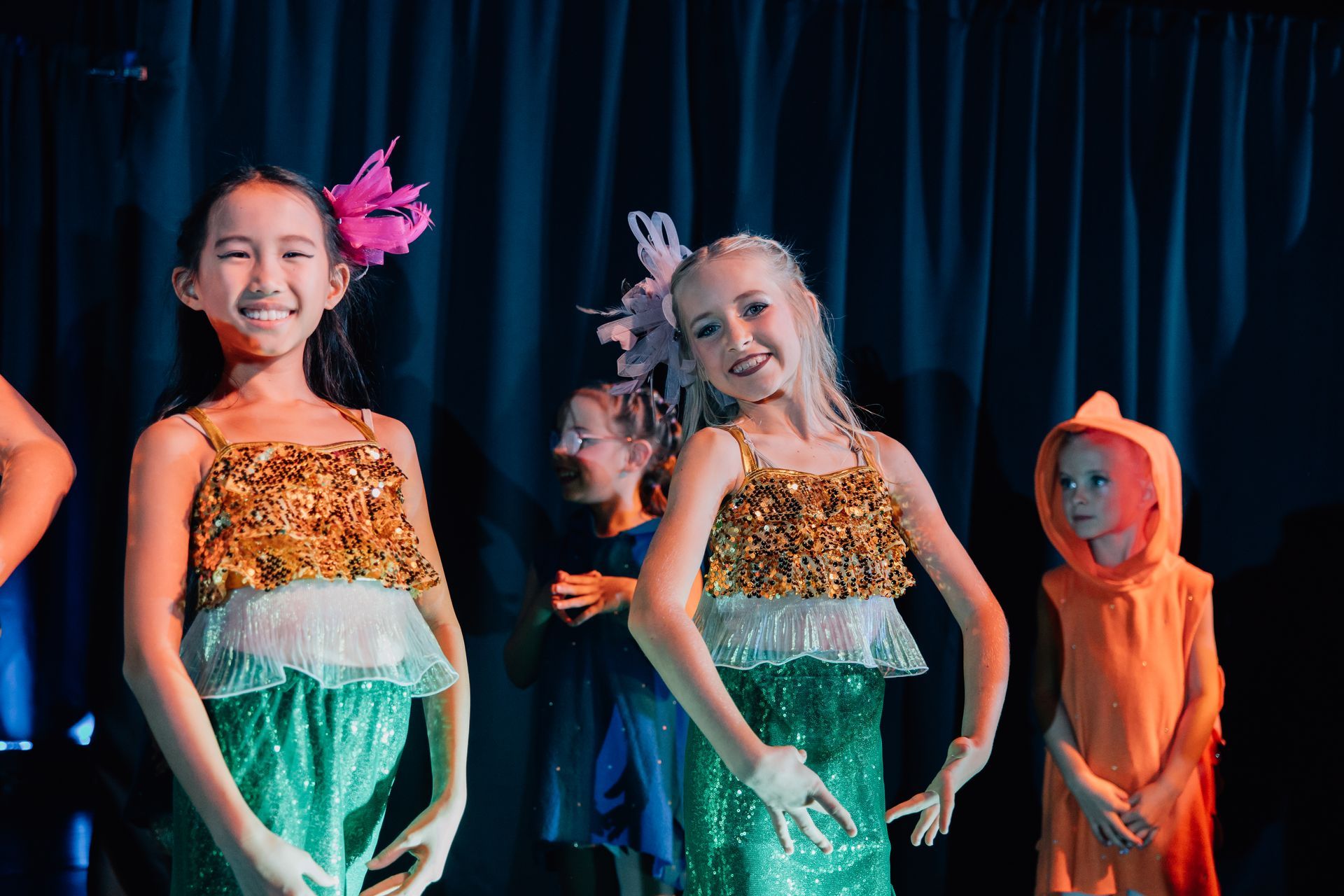 Children in colorful costumes smiling and dancing on stage for the Little Mermaid stage production.