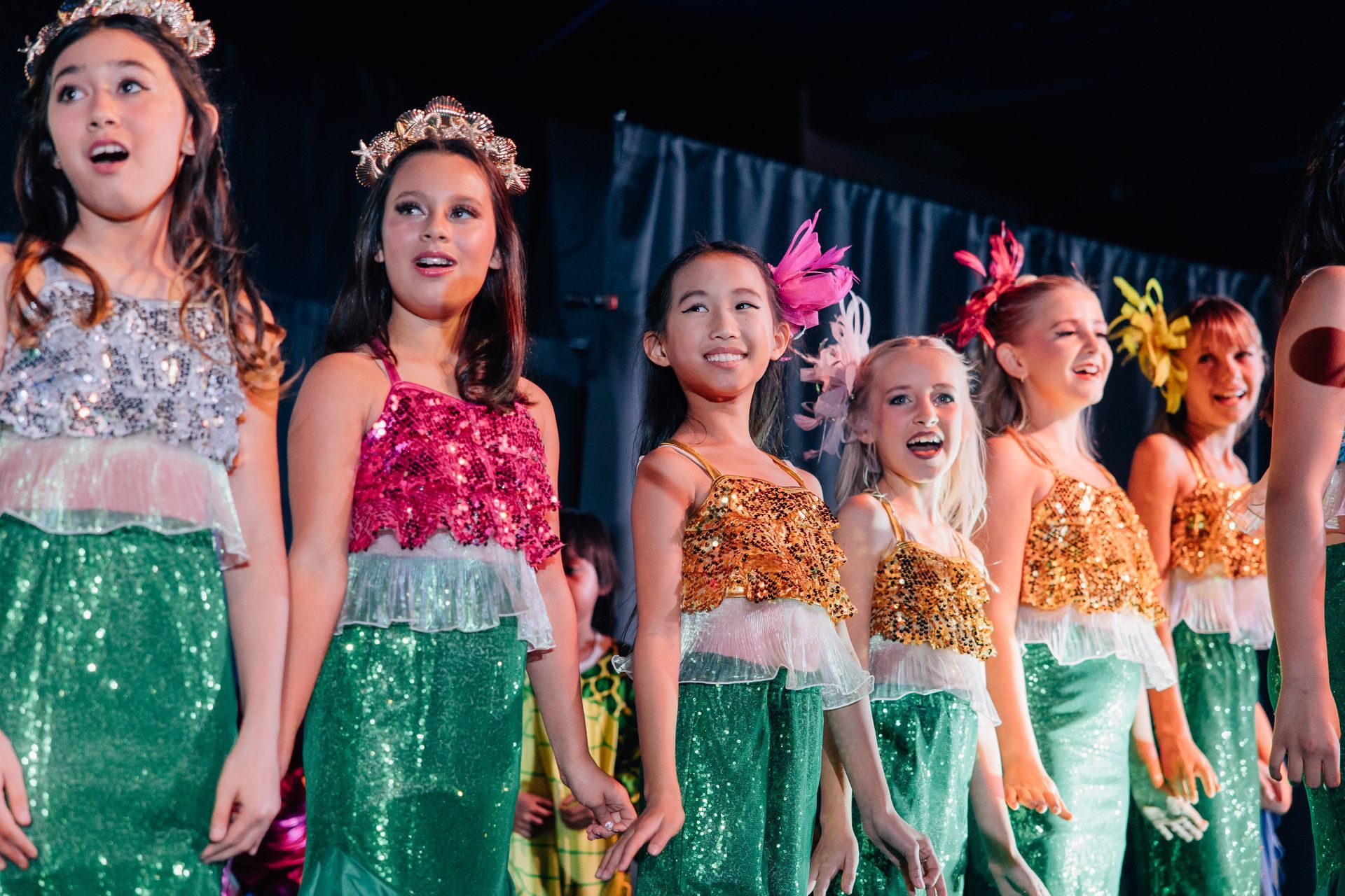 Children in sparkly costumes performing on stage for the Little Mermaid stage production.