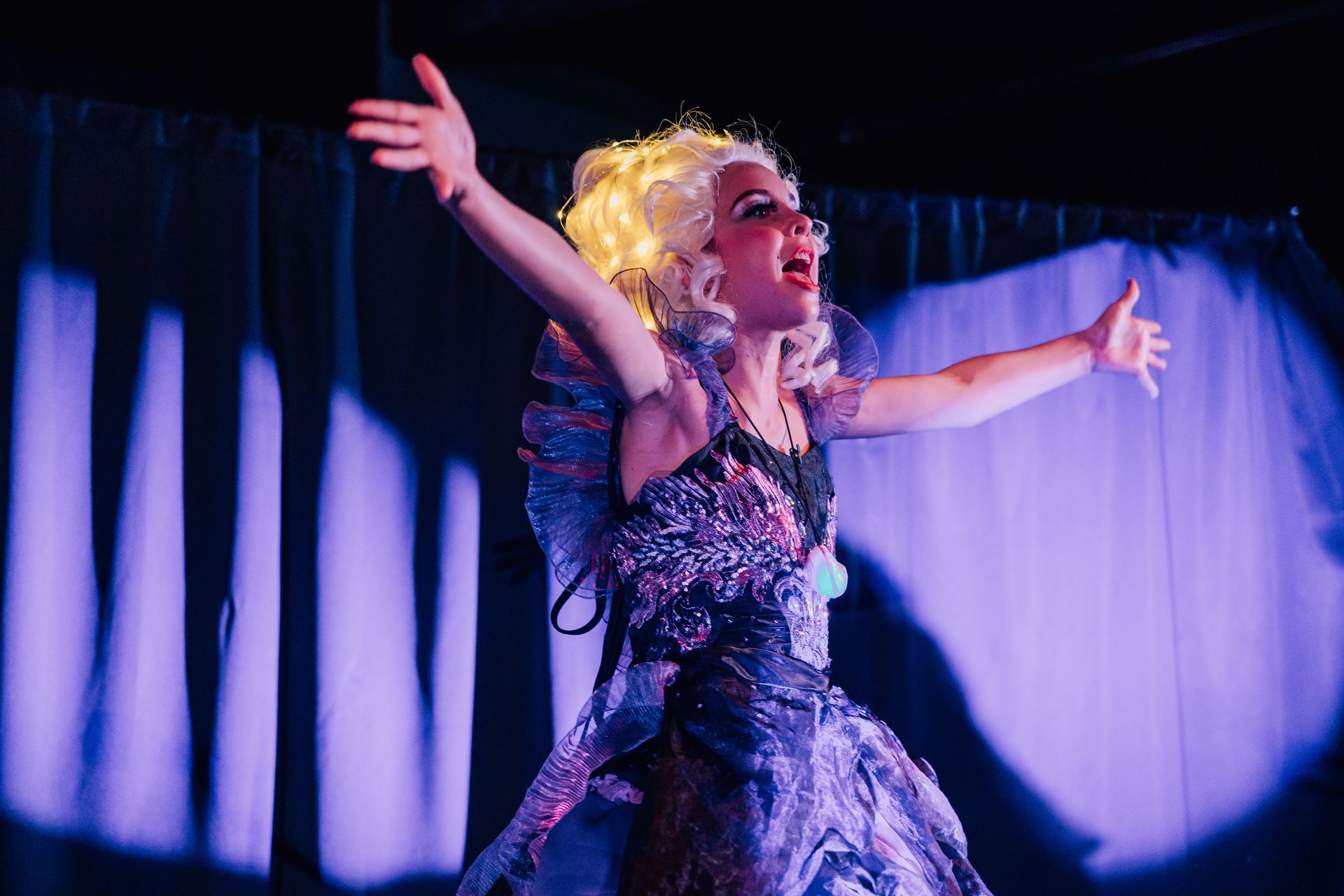 Ursela in a sparkly dress with arms outstretched with purple curtains for the  Little Mermaid stage production.