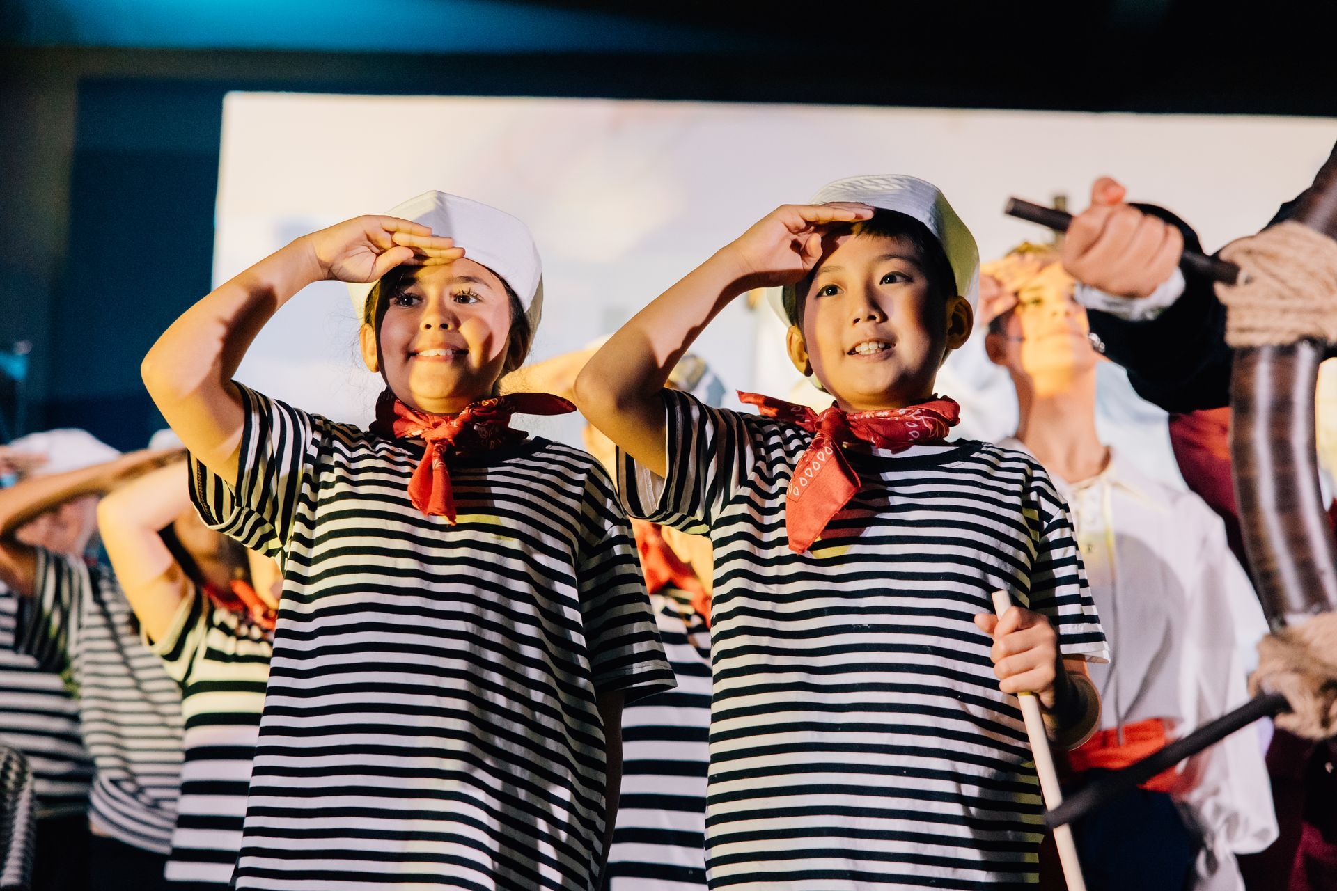 Children in striped shirts and white hats perform on stage, saluting and smiling for the  Little Mermaid stage production.