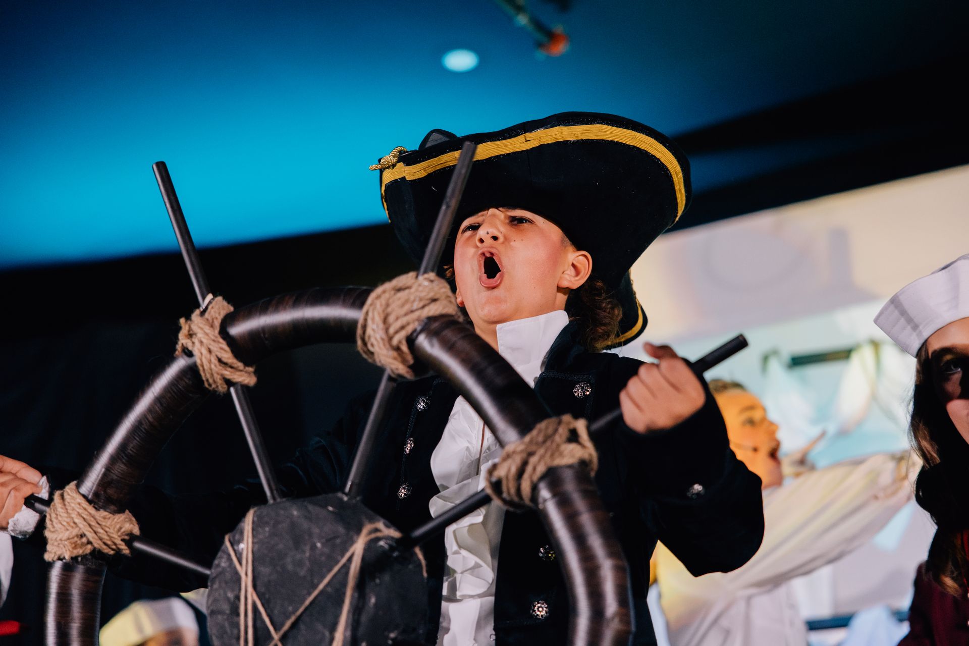 Child in a black tricorn hat playing a drum, mouth open in excitement for the  Little Mermaid stage production.
