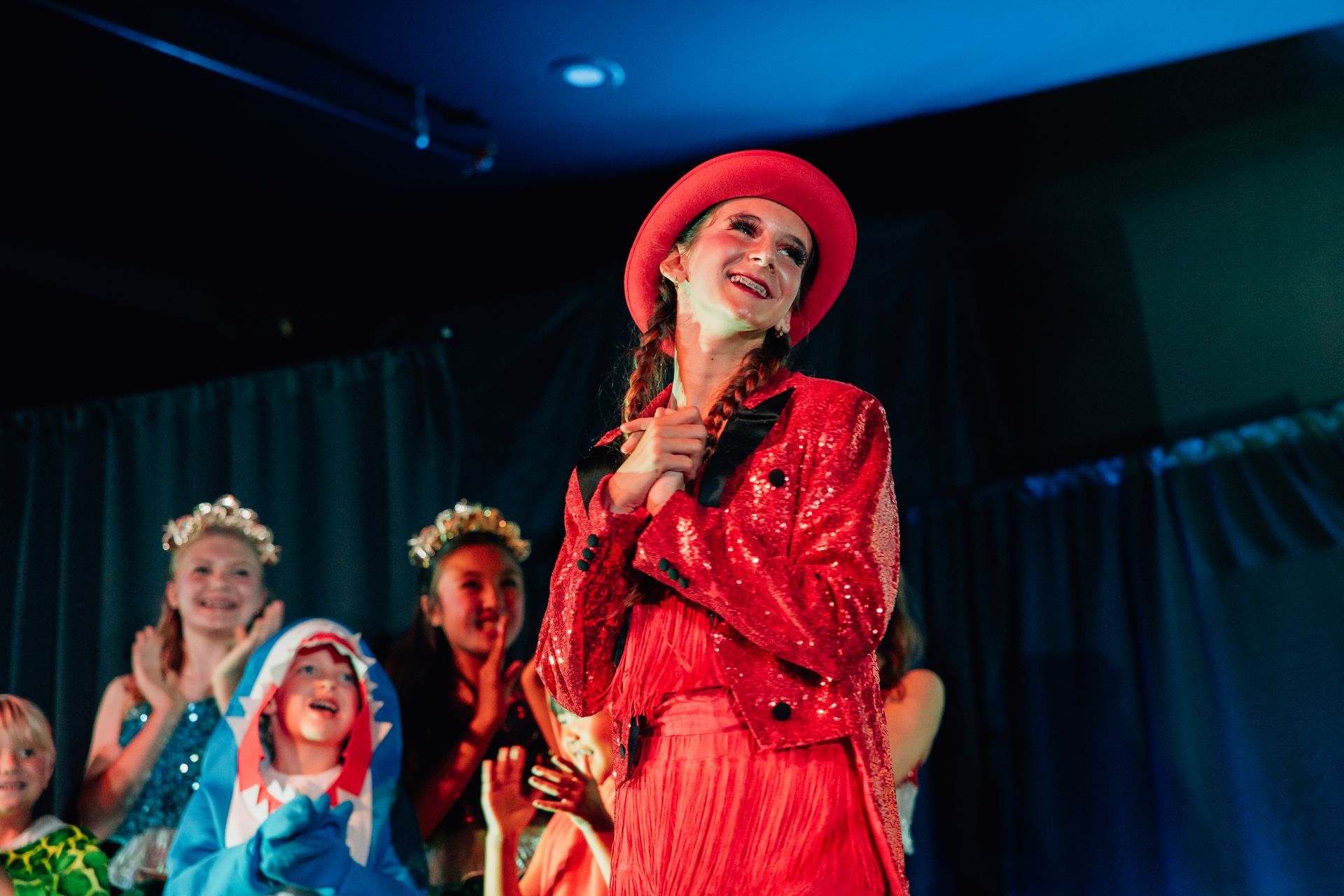 Performer in a red sequined outfit singing on stage for the  Little Mermaid stage production.