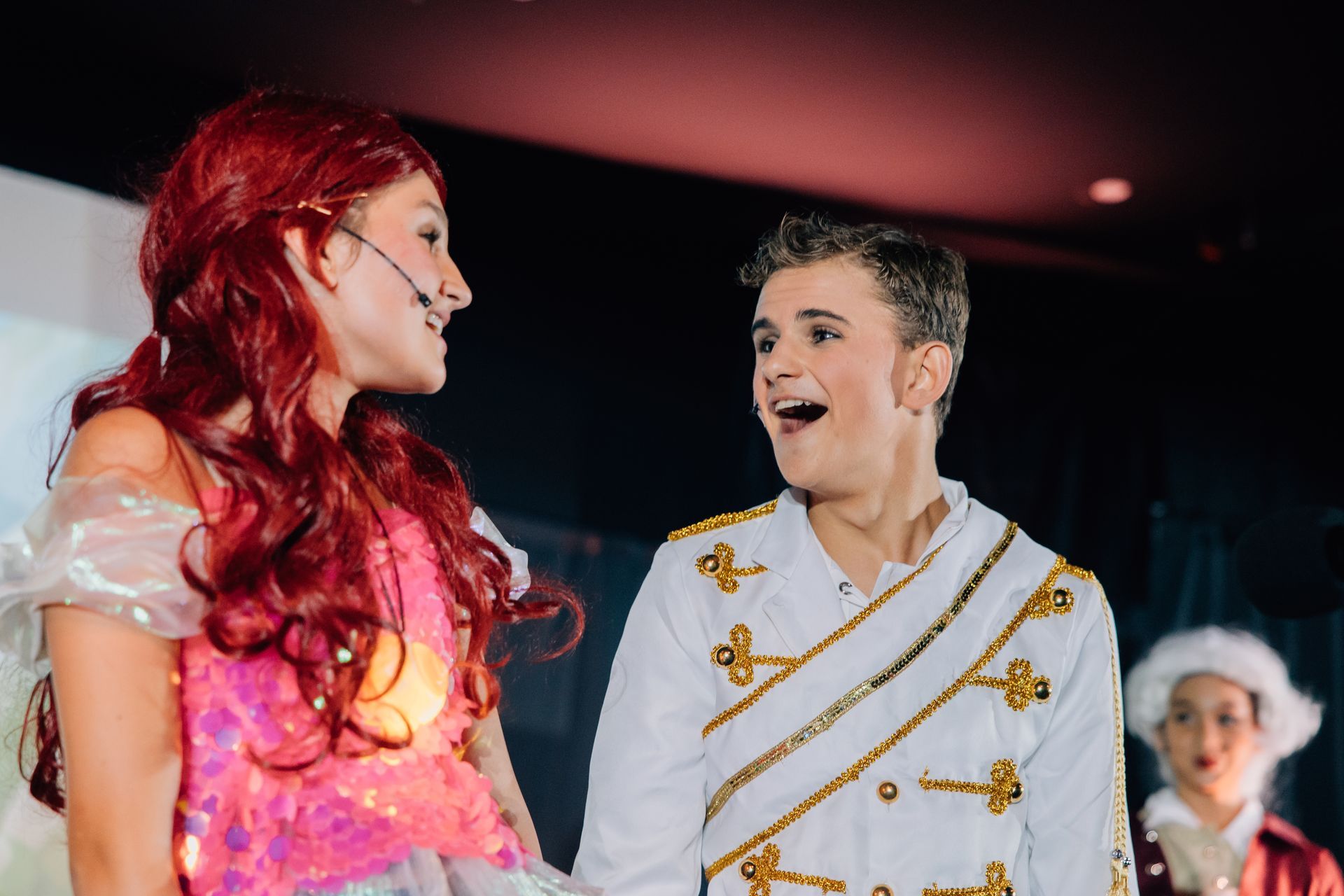Two performers in colorful costumes smiling on stage under theater lights for the  Little Mermaid stage production.