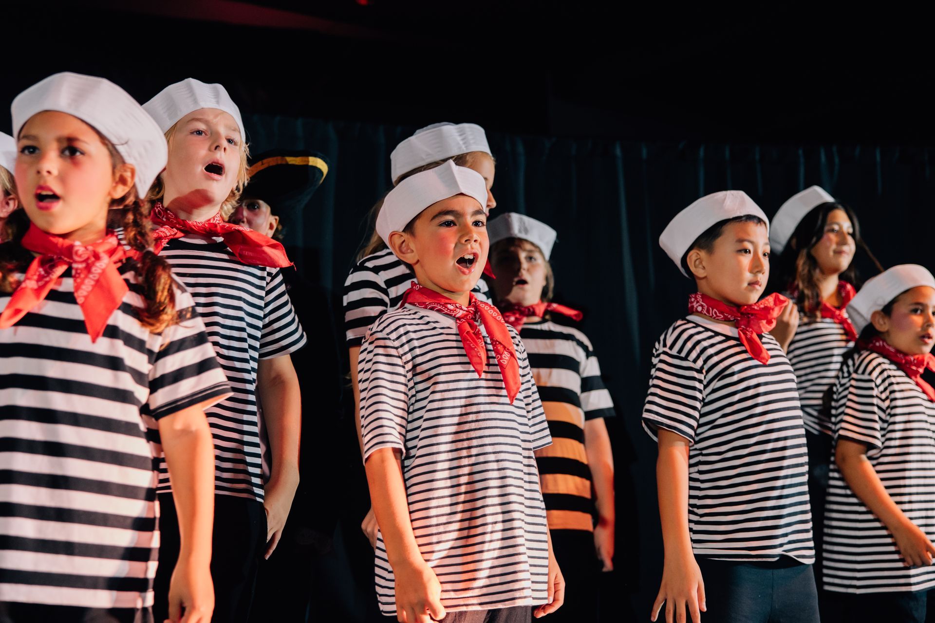 Children in striped shirts and chef hats on stage for the  Little Mermaid stage production at Revolution Theatre Company.