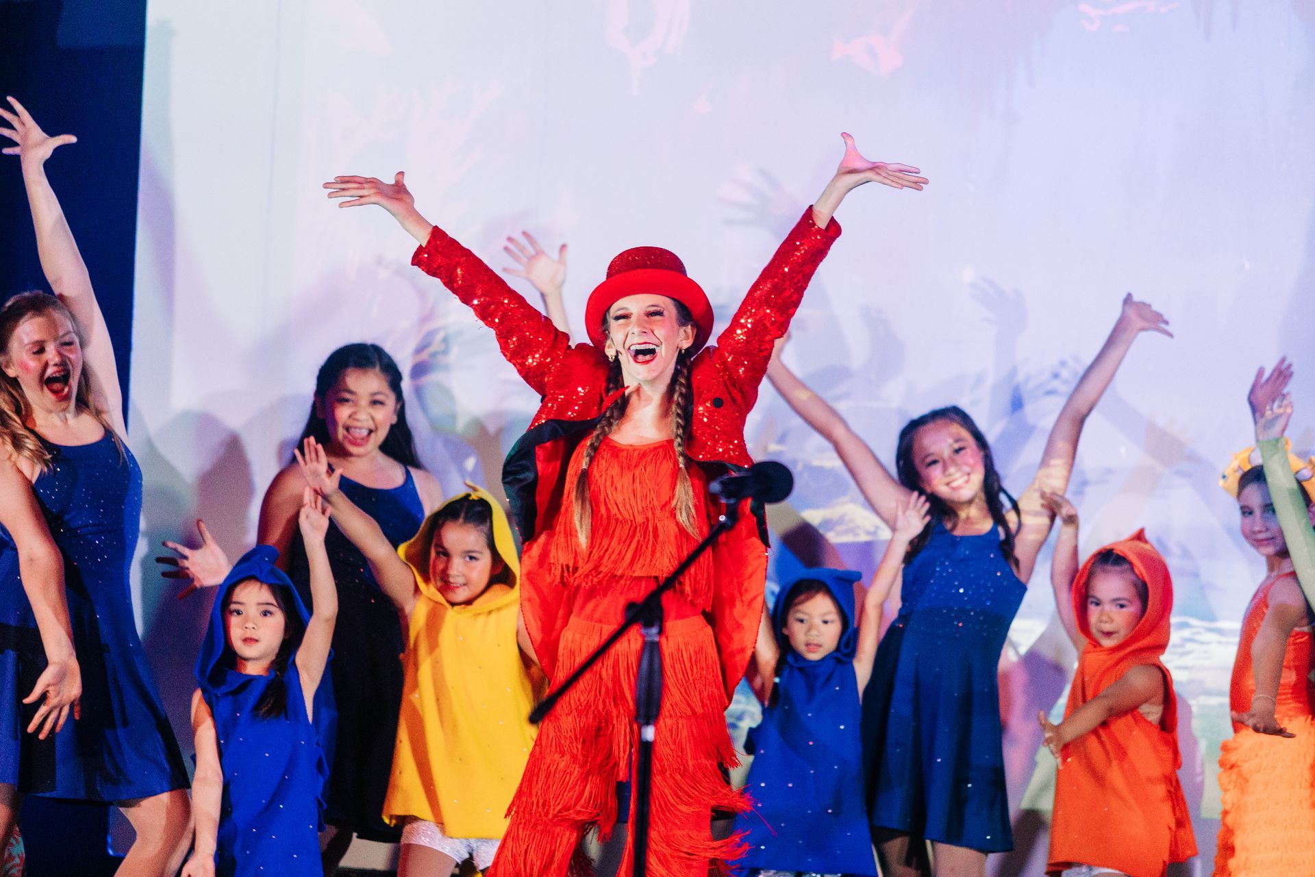 Dancers in colorful outfits pose with arms raised on a stage under bright lights