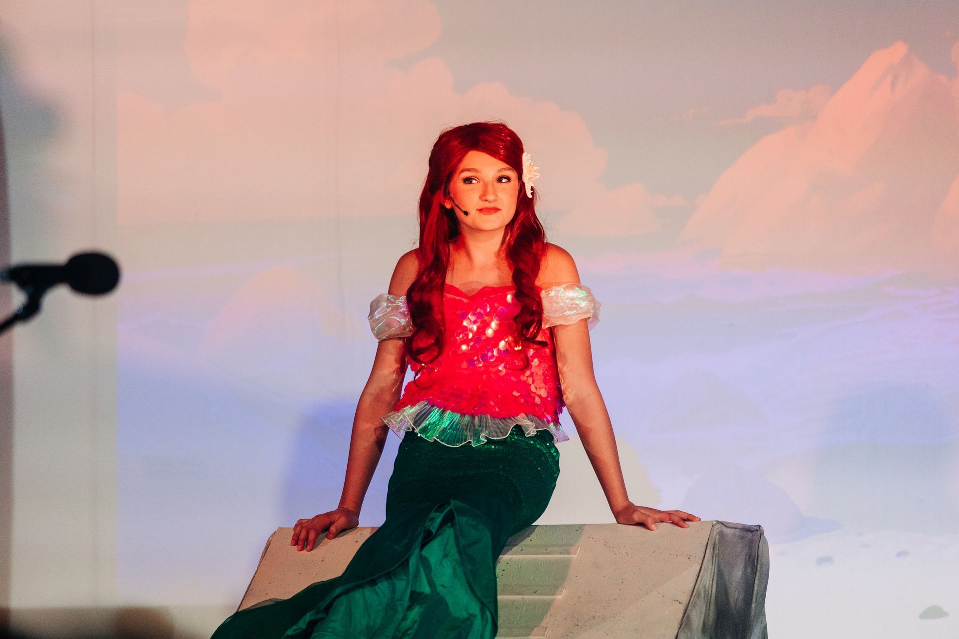 Woman in a red top and green skirt posing on a rock against a pastel sky backdrop
