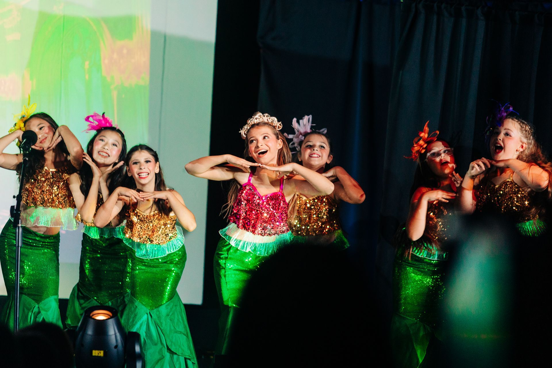 Dancers in green skirts and sparkly tops performing on stage with colorful lighting