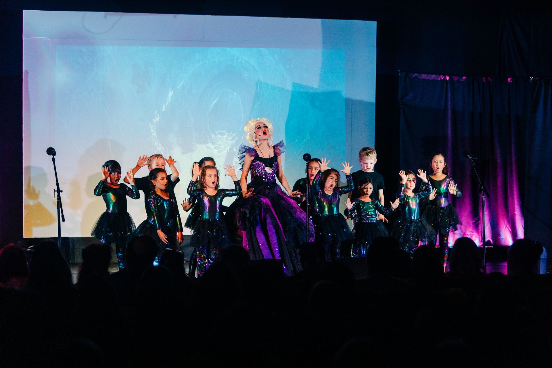 Performers in black and purple costumes onstage under a large screen and purple lights