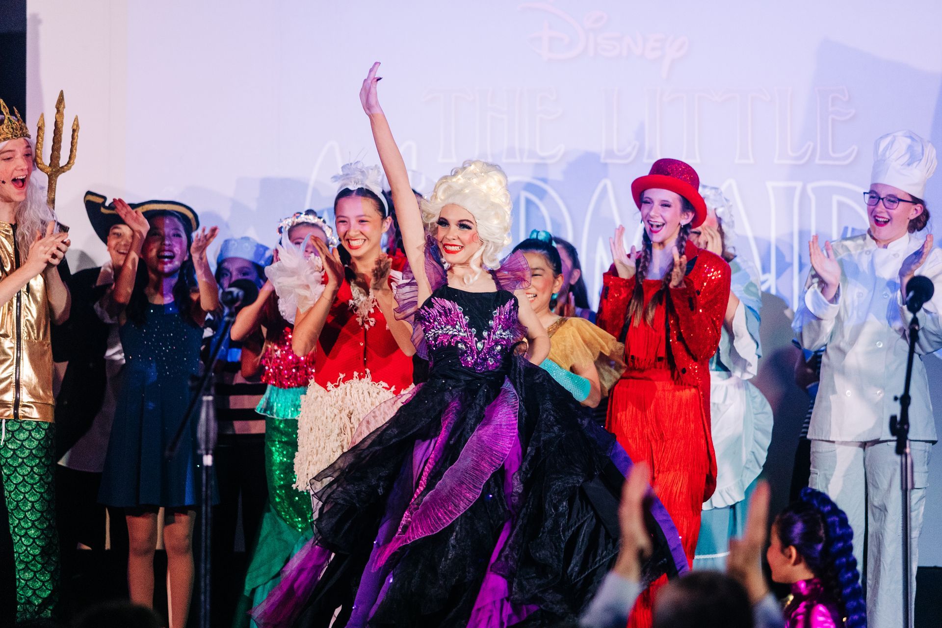 Costumed performers onstage with trophies, posing and cheering at a Disney event