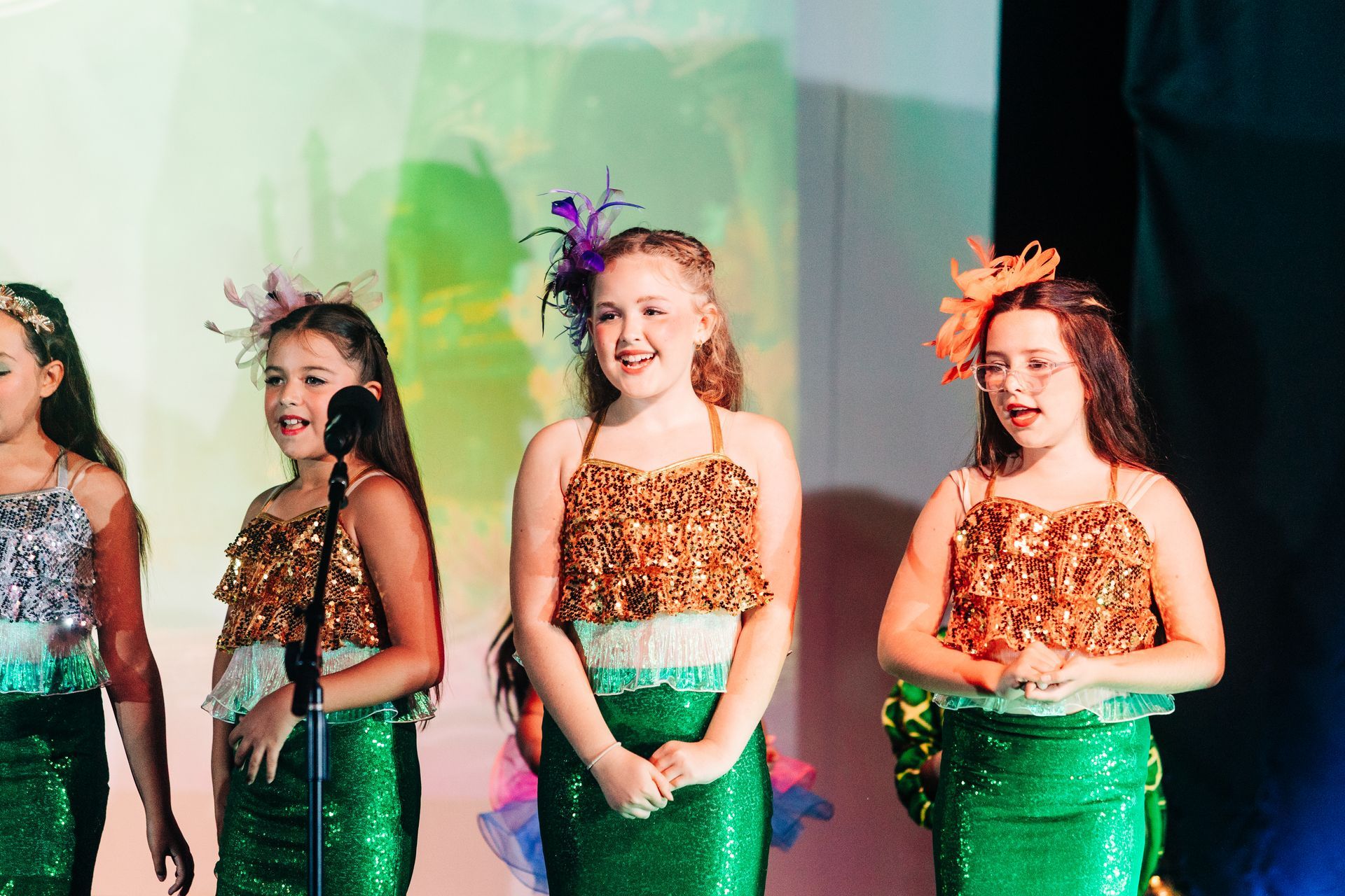 Three children in sparkly costumes performing on stage with colorful lights.