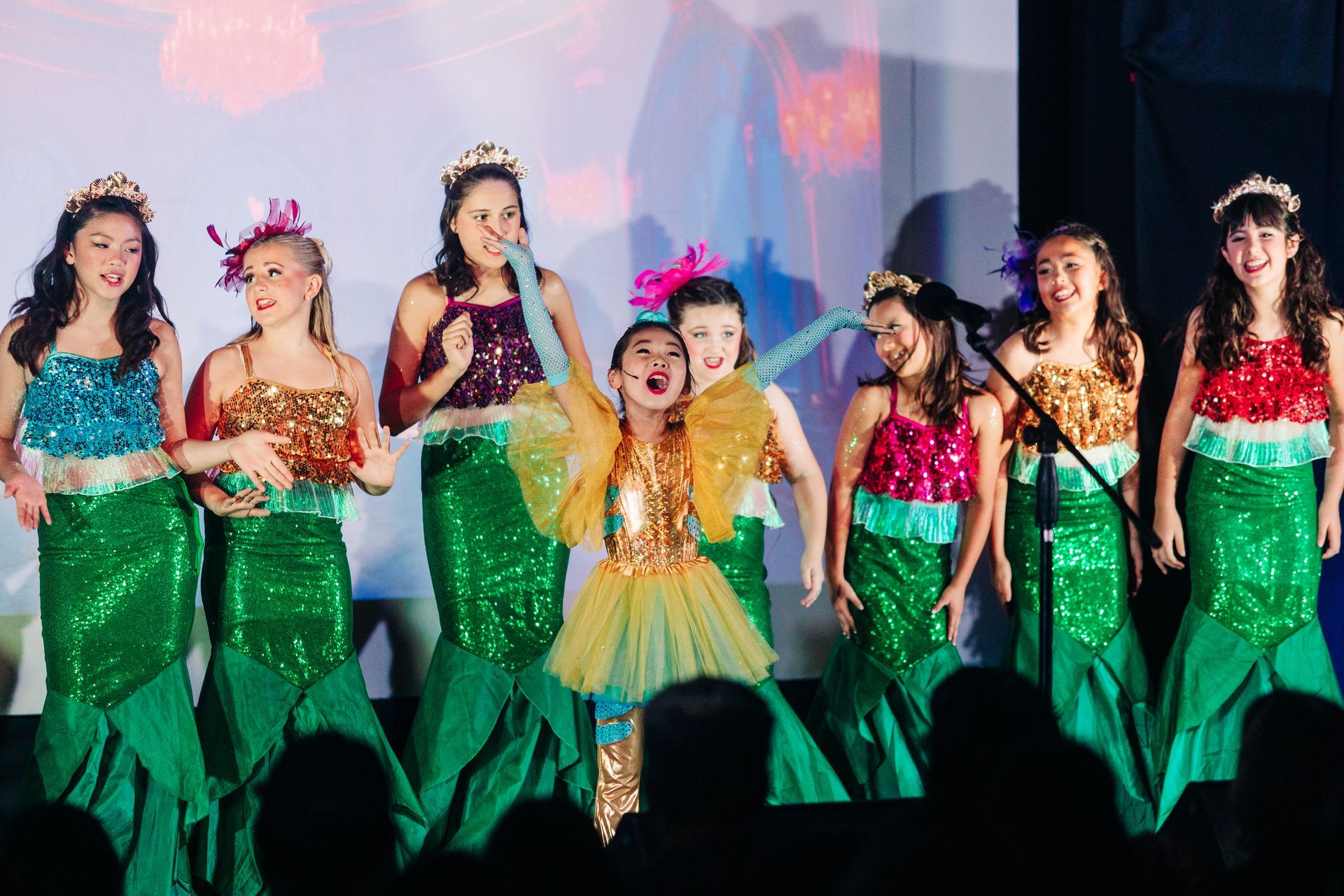 Children in colorful costumes performing a dance on stage under bright lights