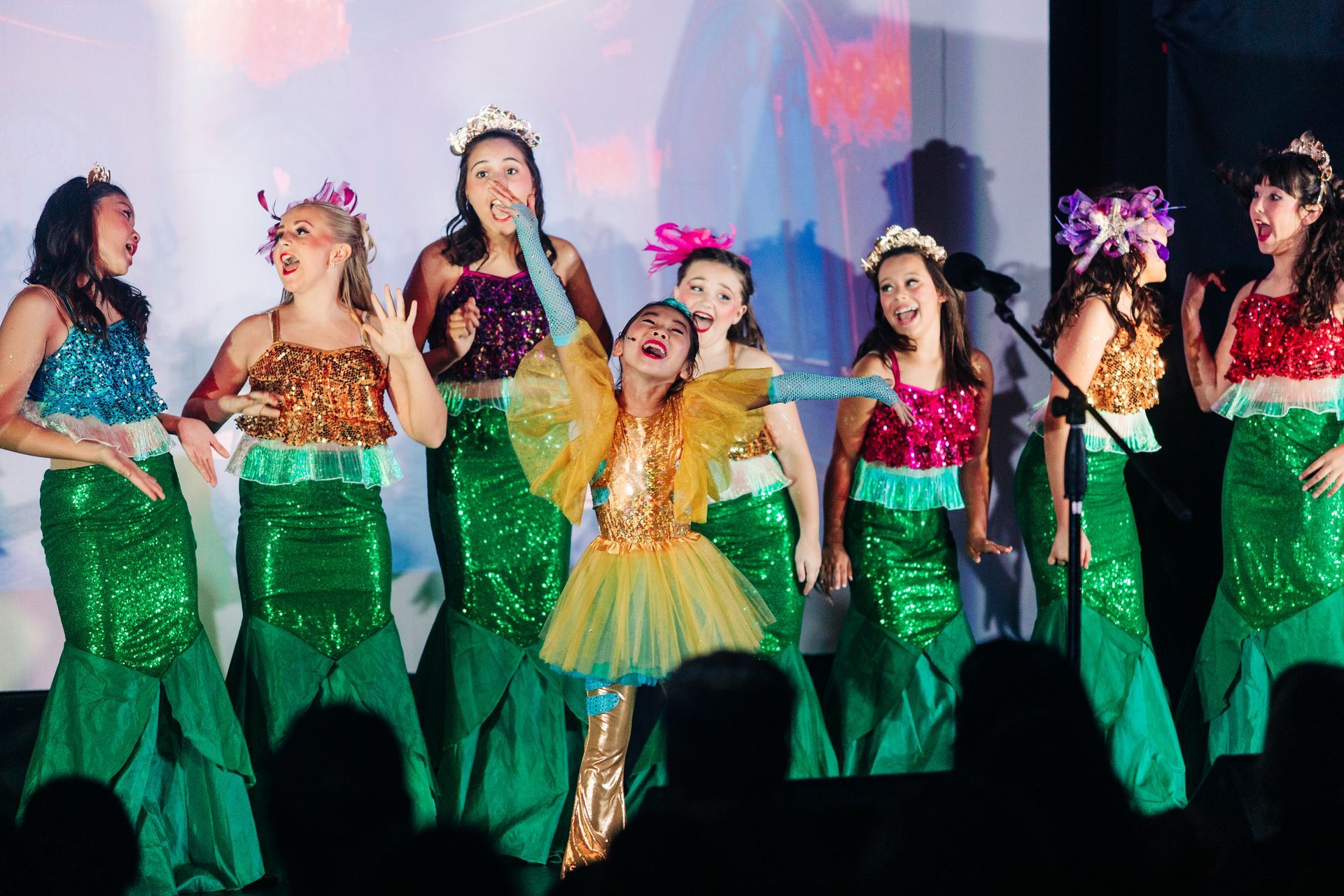 Dancers in colorful costumes performing on stage with green skirts and floral headpieces