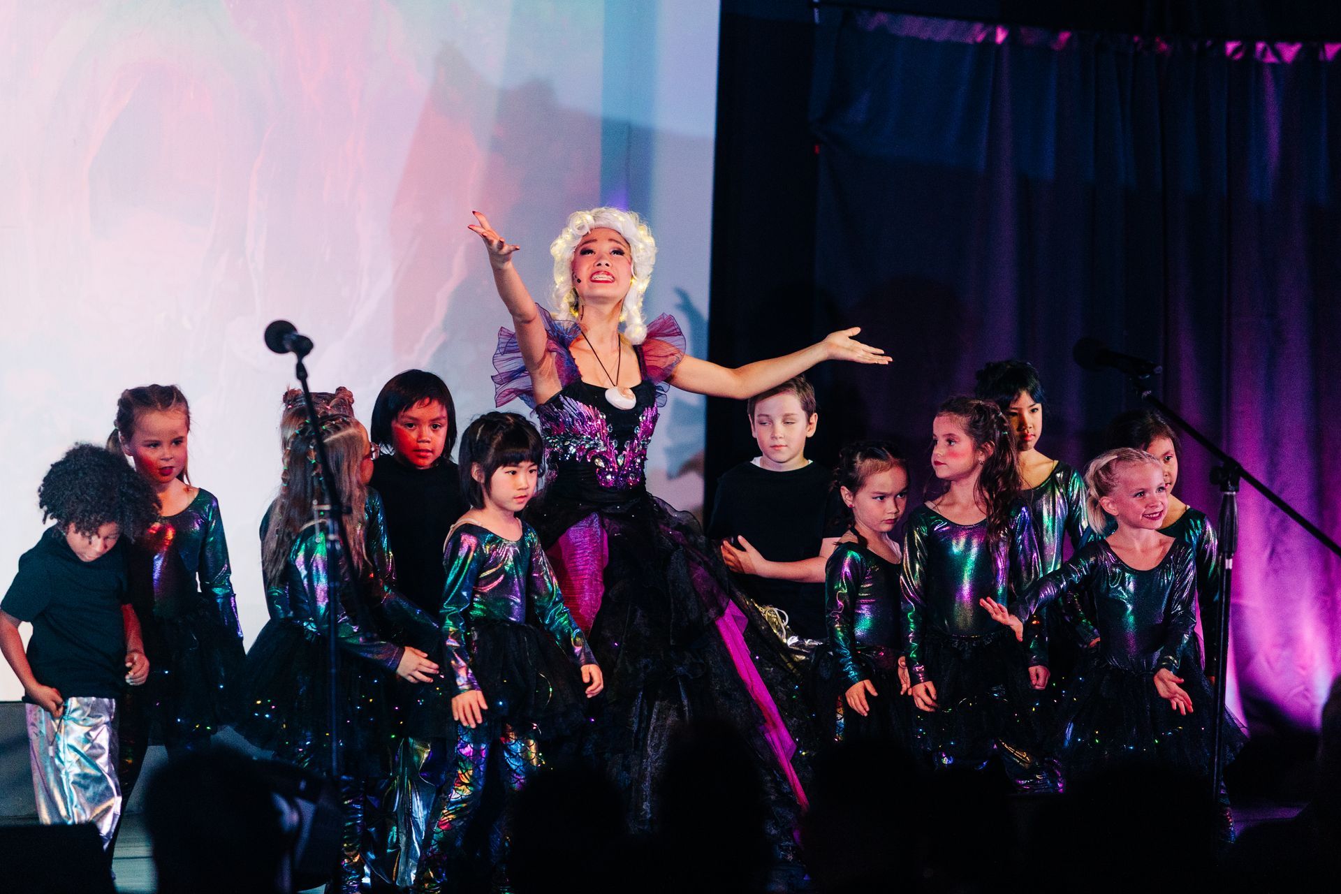 Performers in black costumes dance onstage with a blonde lead singer under pink and purple lights.