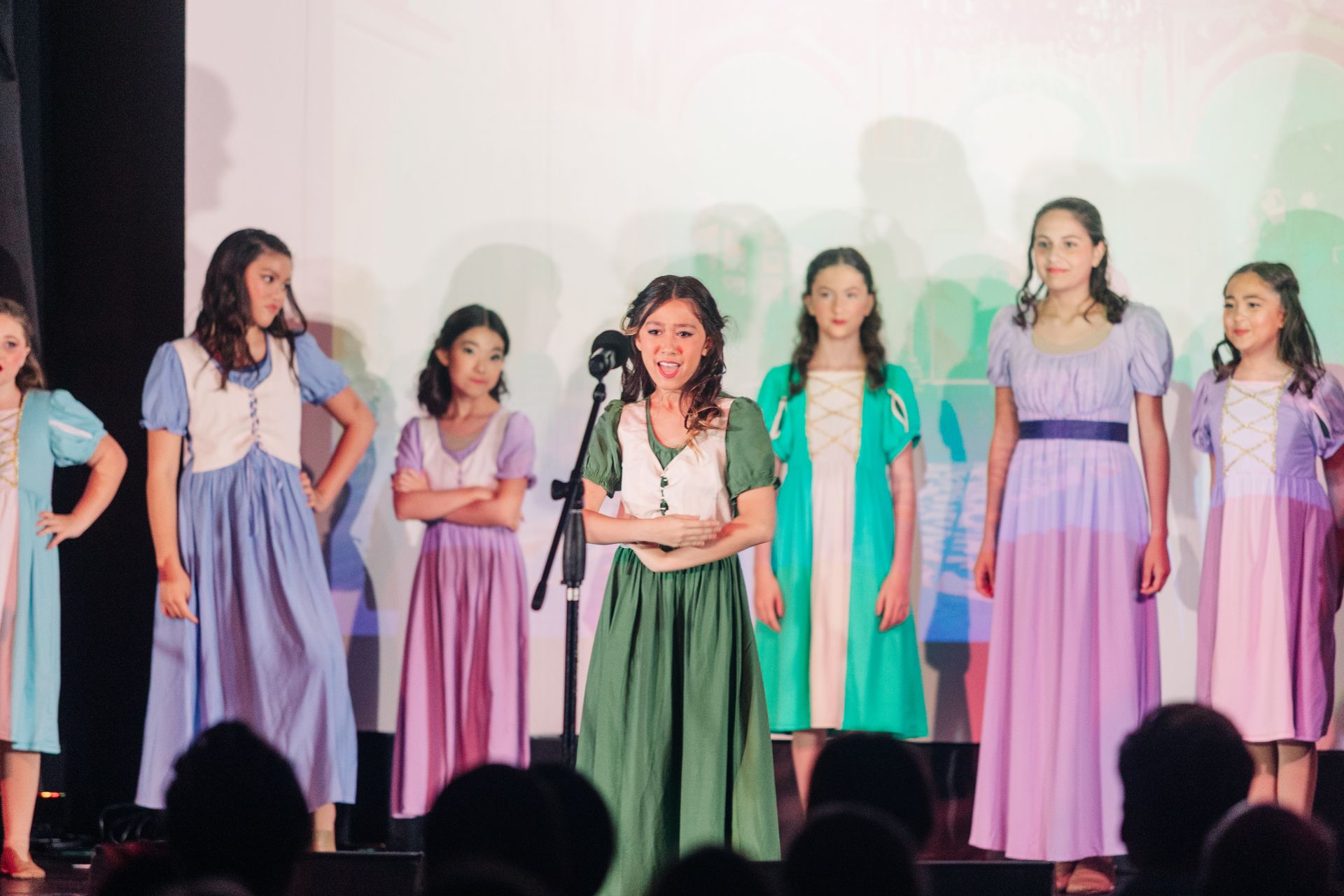 Women in pastel dresses singing onstage with microphones under soft colored lights