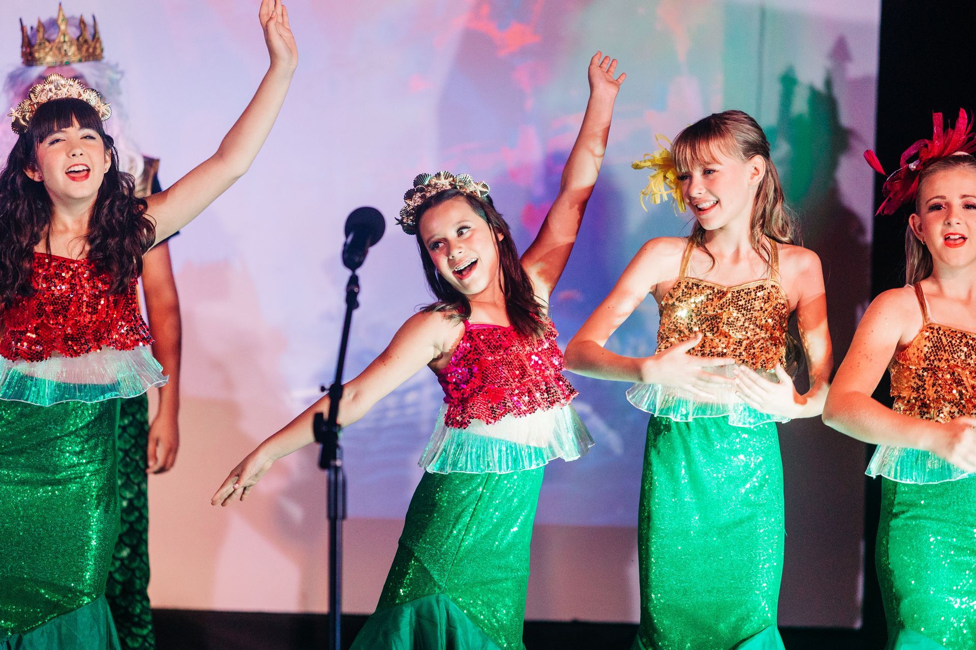 Four dancers in red tops and green skirts performing on stage with raised arms