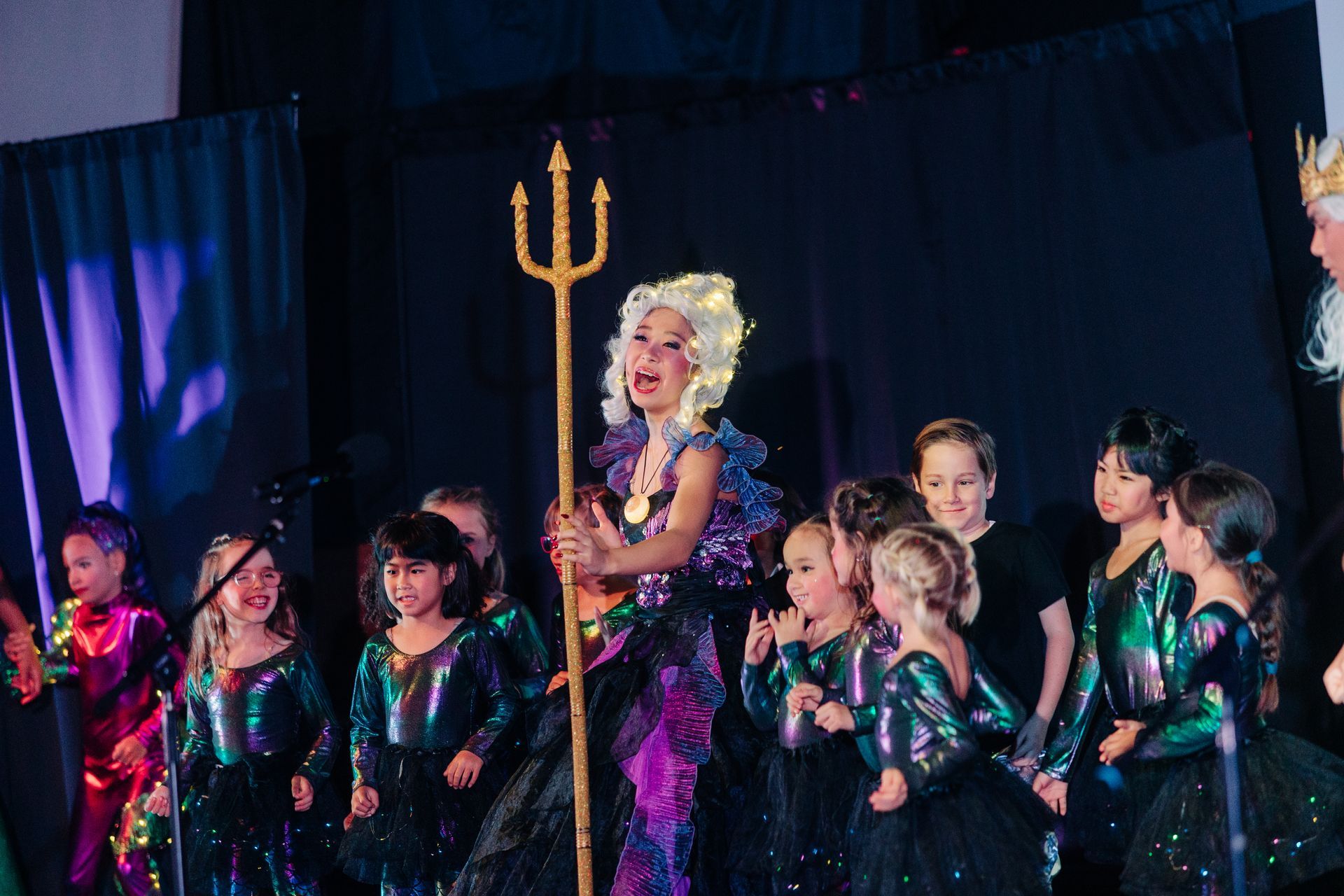 Costumed performers on stage with a person dressed as a mermaid holding a golden trident
