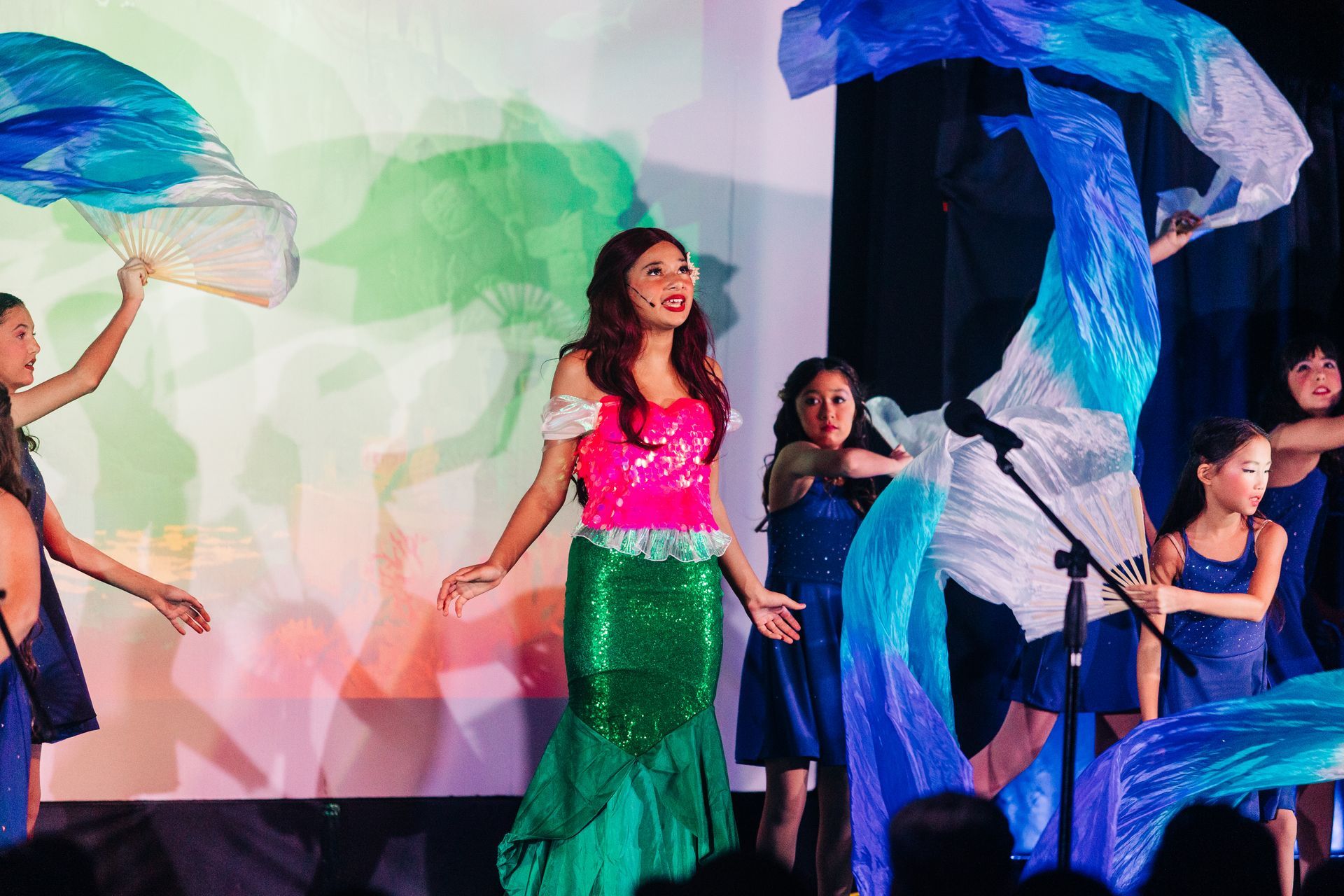 Performers with colorful umbrellas dancing on stage in bright costumes