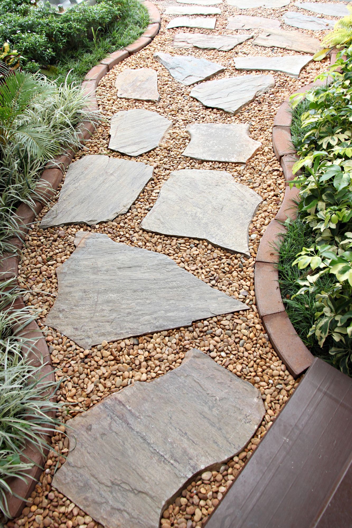 Stepping-stone garden path with irregular stone slabs and tan gravel bordered by plants and edging