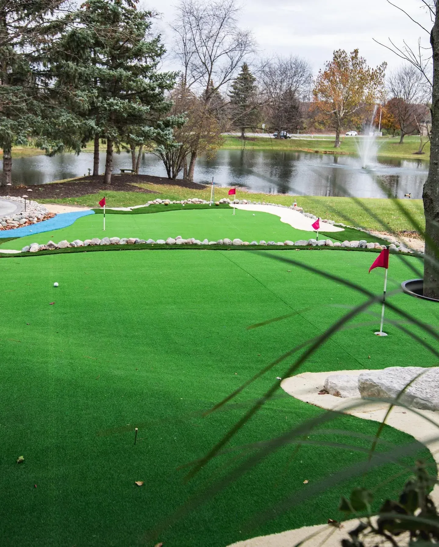 Miniature golf course with green turf, red flags, and a water feature in the background.
