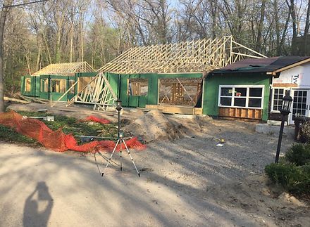 Construction site: House under construction; wooden frame, green siding, surrounded by trees and orange safety fencing.