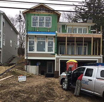 House under construction with green siding, deck, and garage. A person stands near a truck.