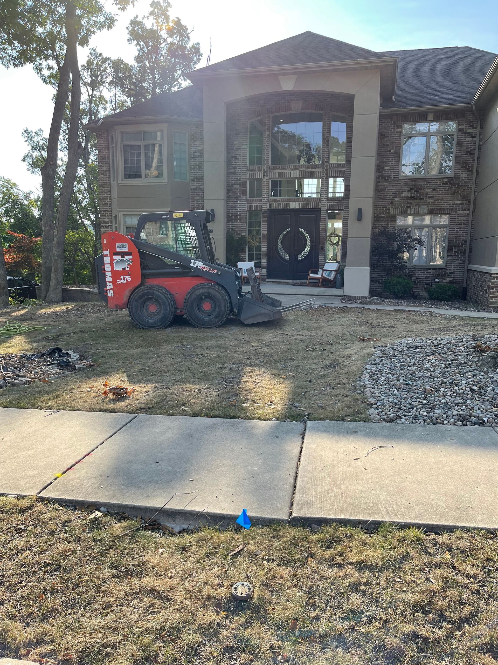 Bobcat in front yard of a two-story house with landscaping in progress.