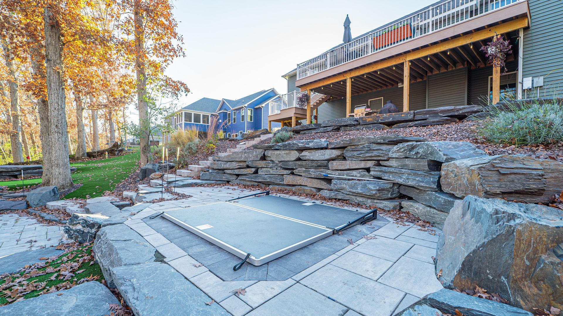 Hot tub with cover, built into patio with stone retaining wall, near a deck.