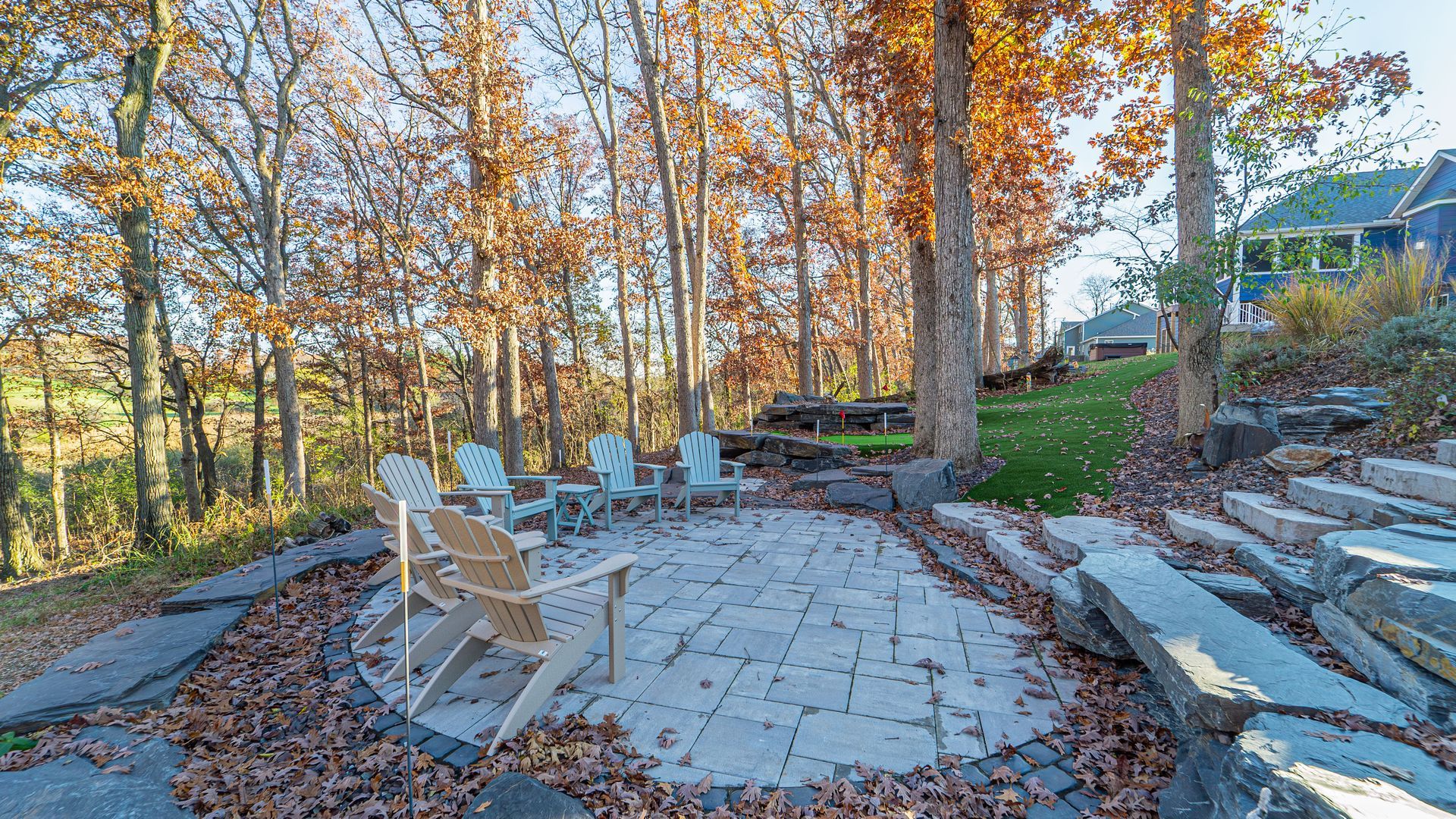 Stone patio with Adirondack chairs surrounded by autumn trees.