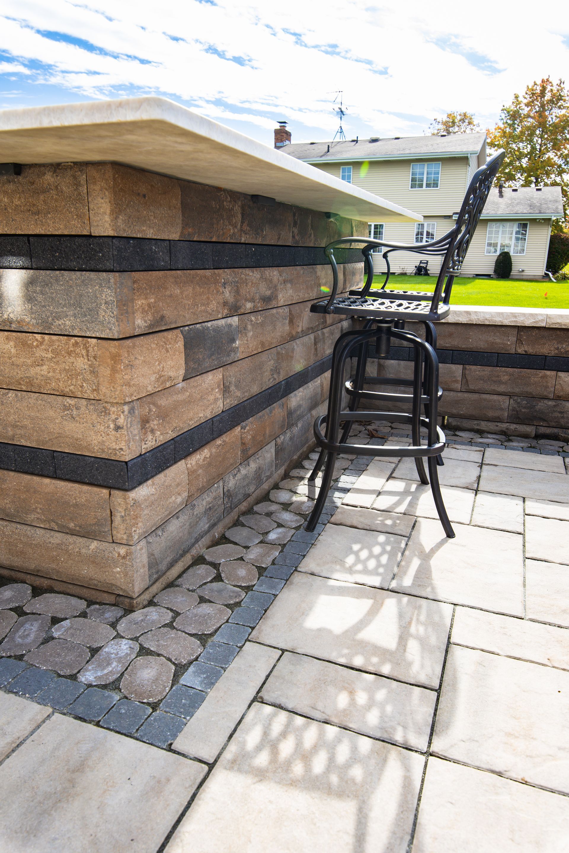 Outdoor bar made of stone blocks with a black metal stool and patio pavers.
