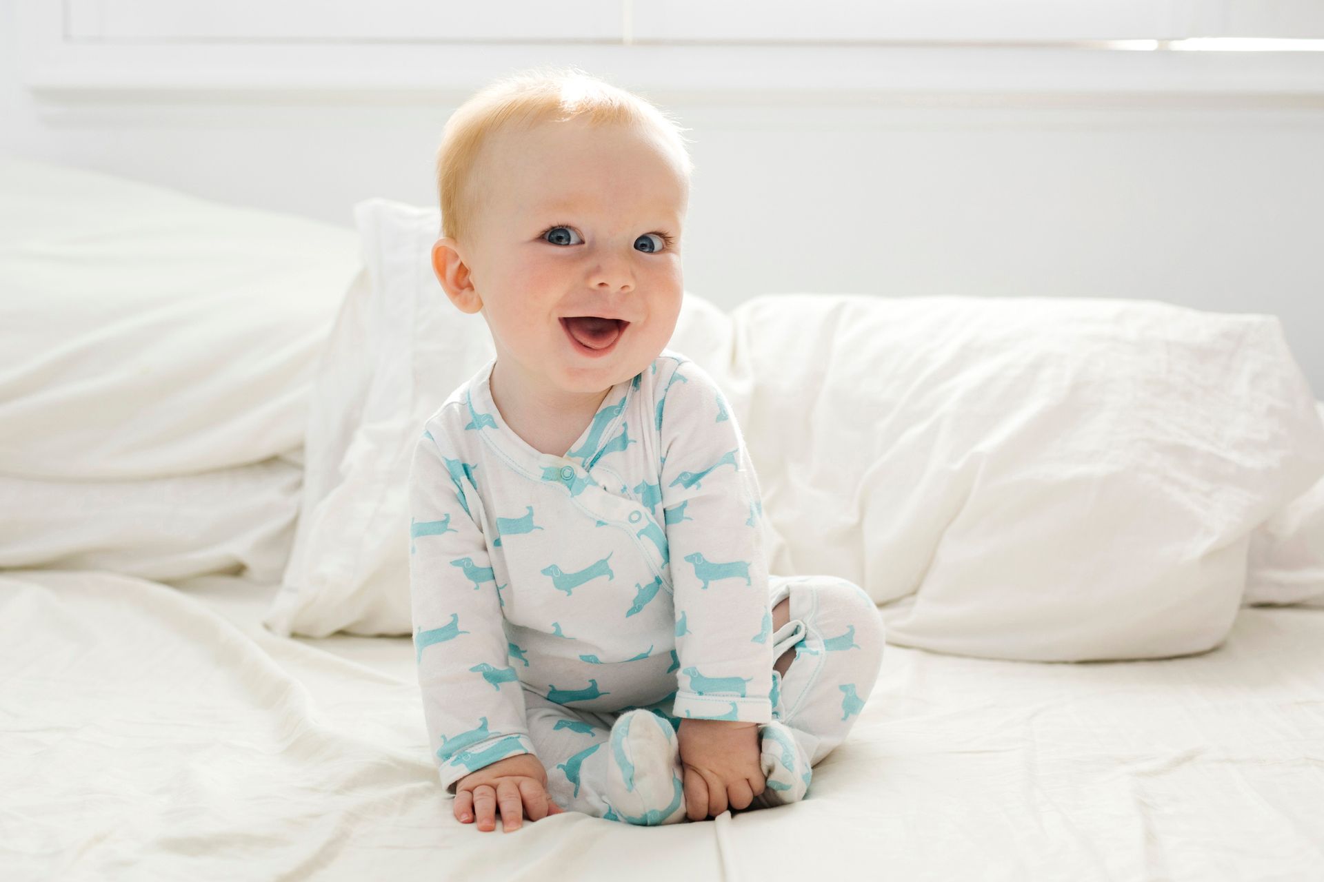 Un bambino è seduto su un letto, indossa il pigiama e sorride.