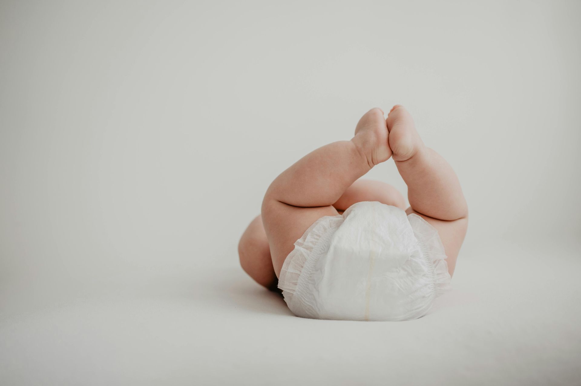 Un neonato con il pannolino è sdraiato sulla schiena su una superficie bianca.