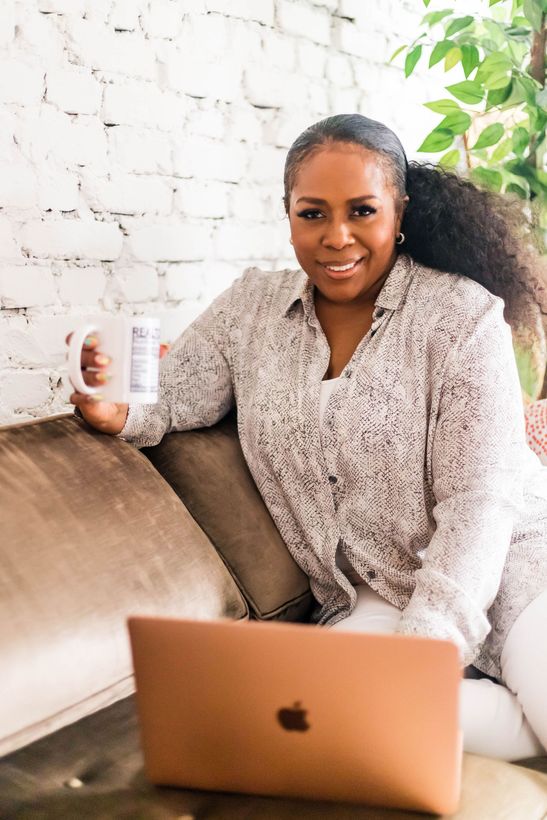 A woman is sitting at a desk with a laptop and a vase of flowers.