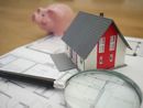 A model house, a piggy bank, and a magnifying glass resting on top of architectural blueprints.
